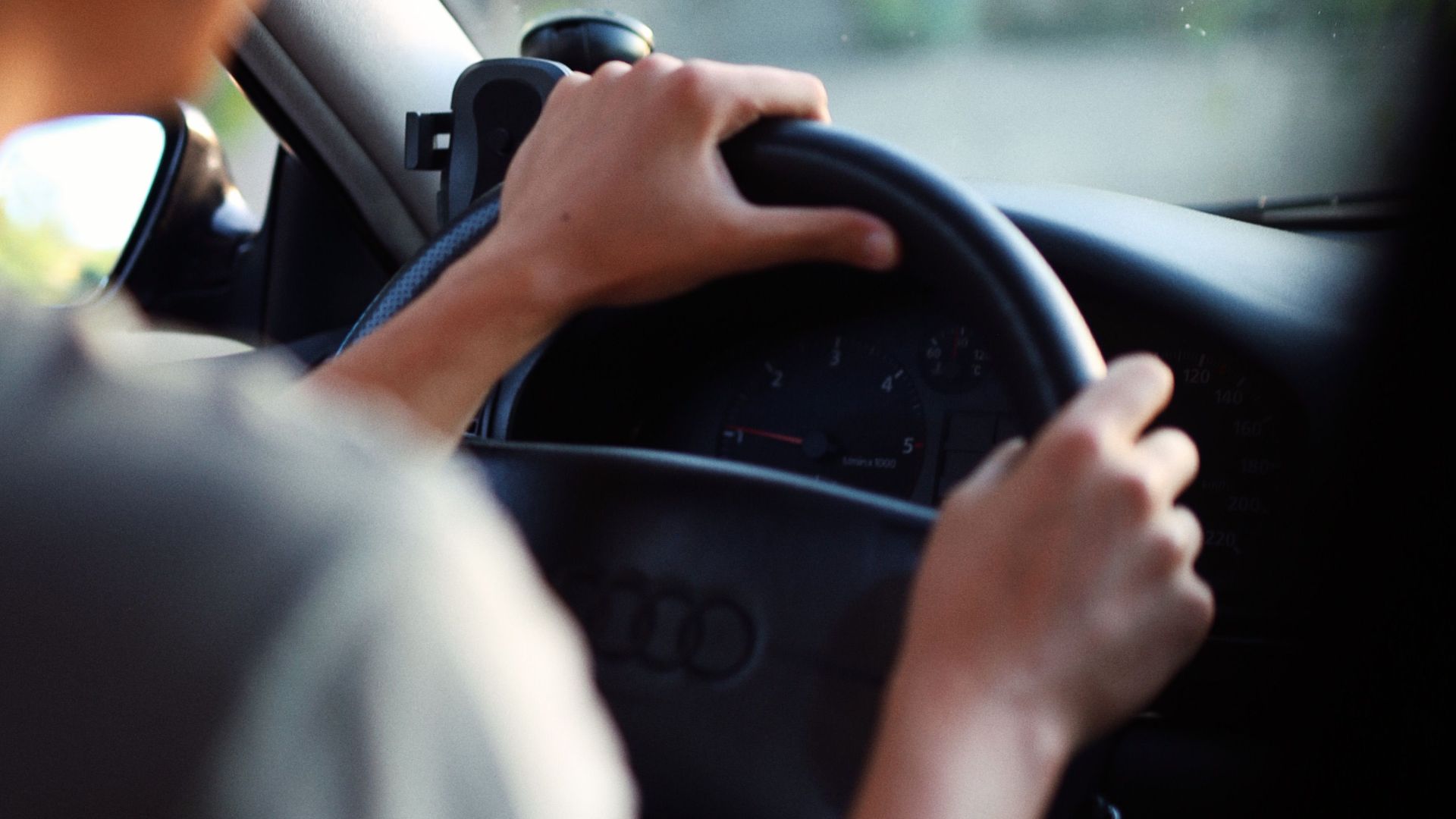 Close-up of a person driving an Audi car showcasing hands on the steering wheel and dashboard view.