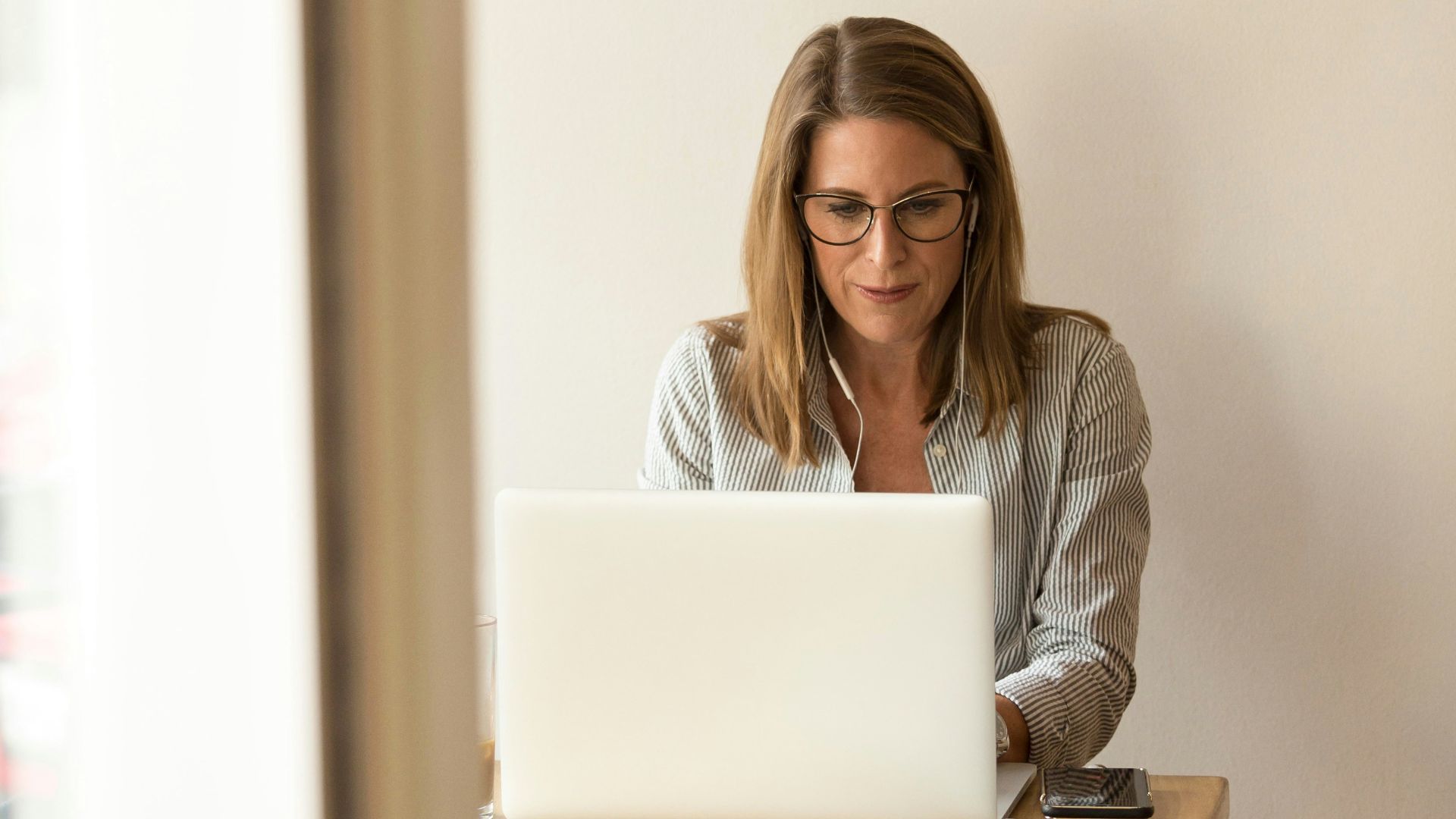woman wearing grey striped dress shirt sitting down near brown wooden table in front of white laptop computer