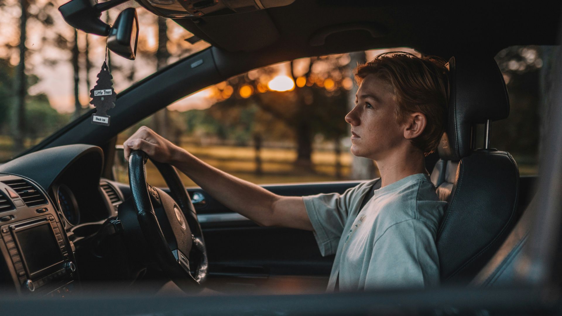 a man sitting in a car with his hand on the steering wheel