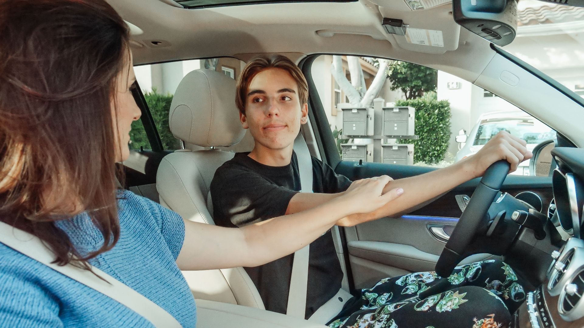 A mother supports her teenage son as he learns to drive in a car