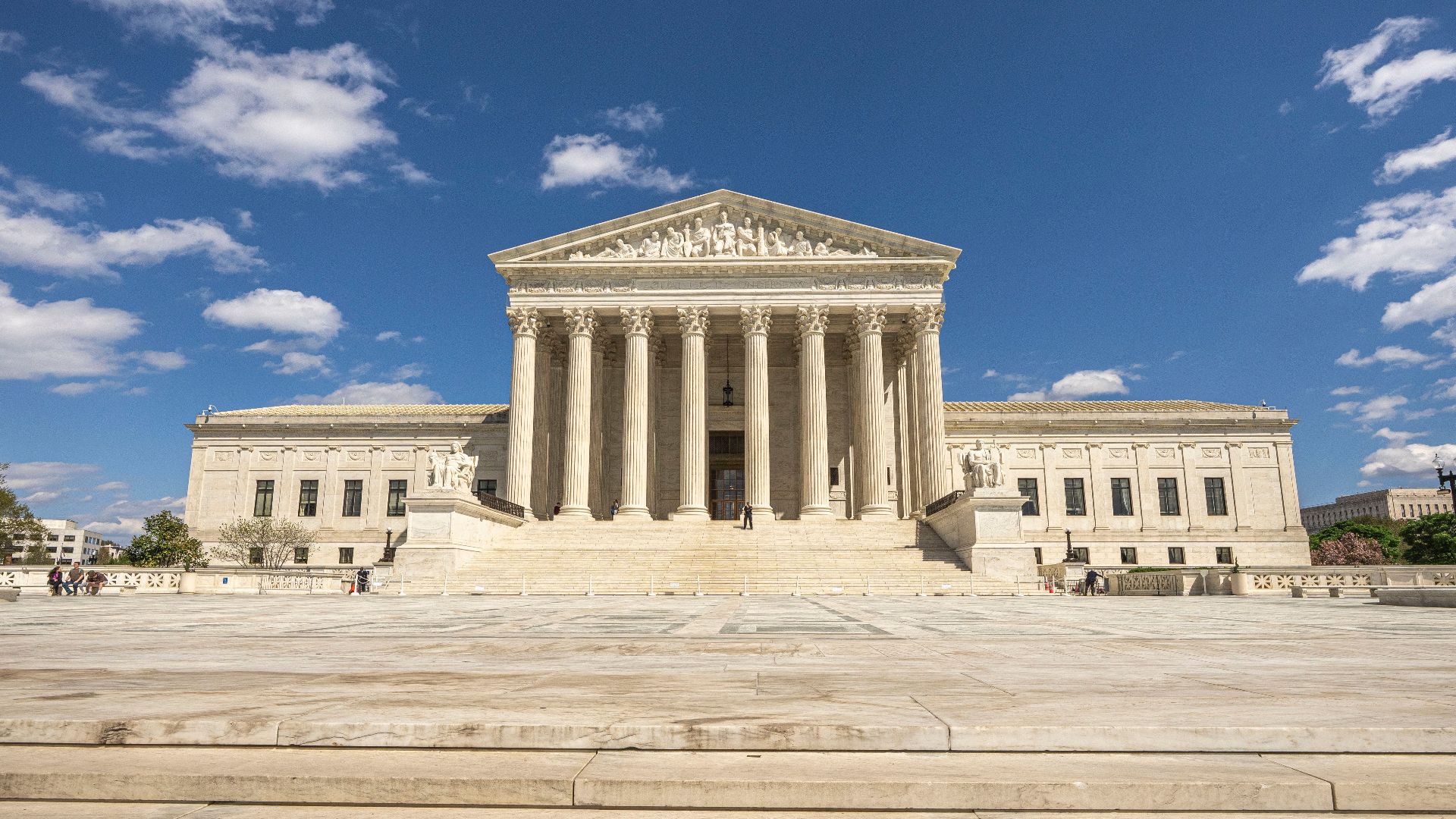 Front view of the United States Supreme Court building on a sunny day with blue sky and clouds.
