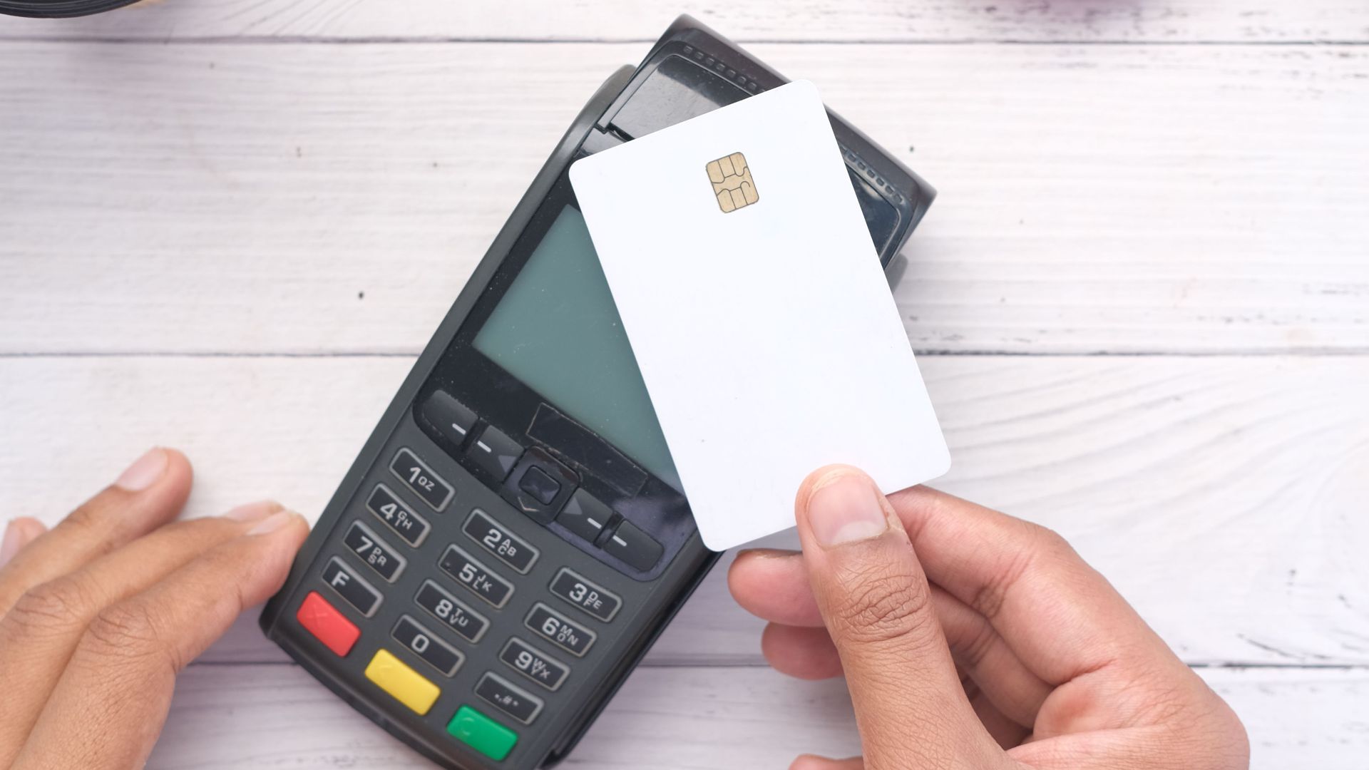 Hands making a contactless payment with a credit card on a wooden table.