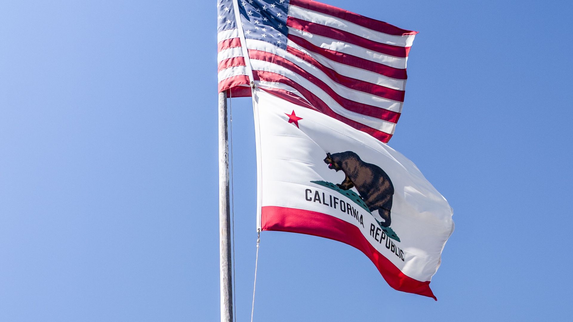 A clear blue sky frames the American and California flags waving atop a flagpole.