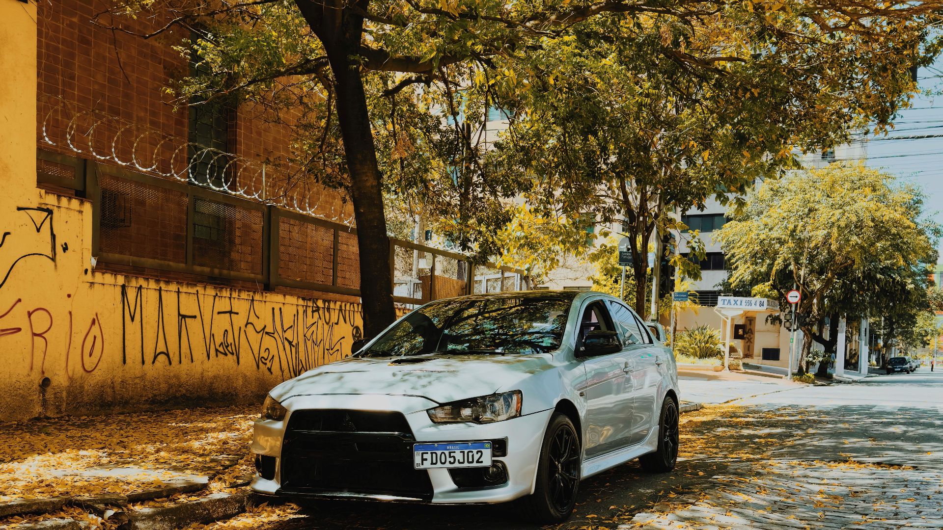 Mitsubishi Lancer parked under tree on cobblestone street in Vila Cordeiro, São Paulo.