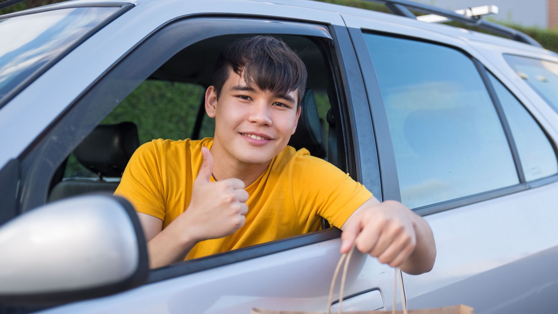 Smiling courier in car delivering a paper bag, offering friendly service.
