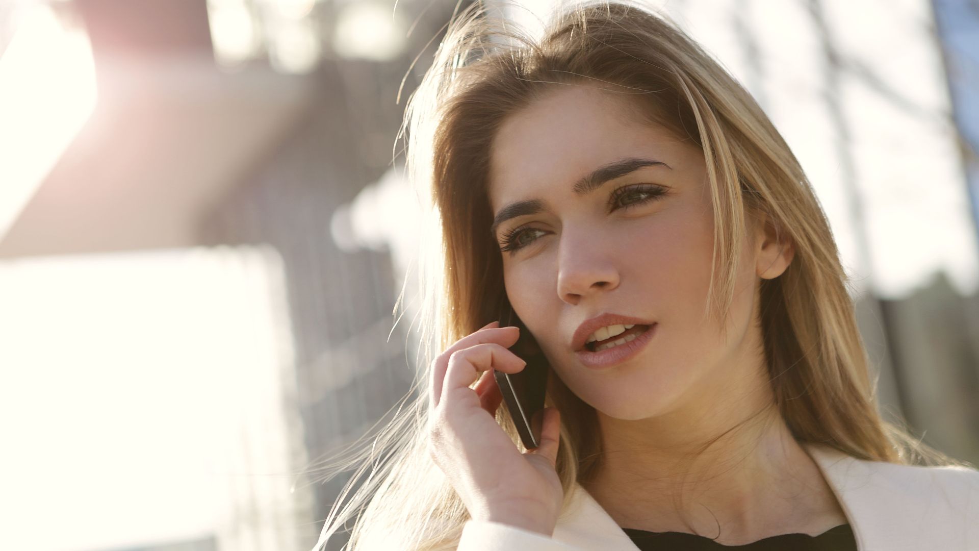 A young woman with blond hair using a smartphone outside on a sunny day.