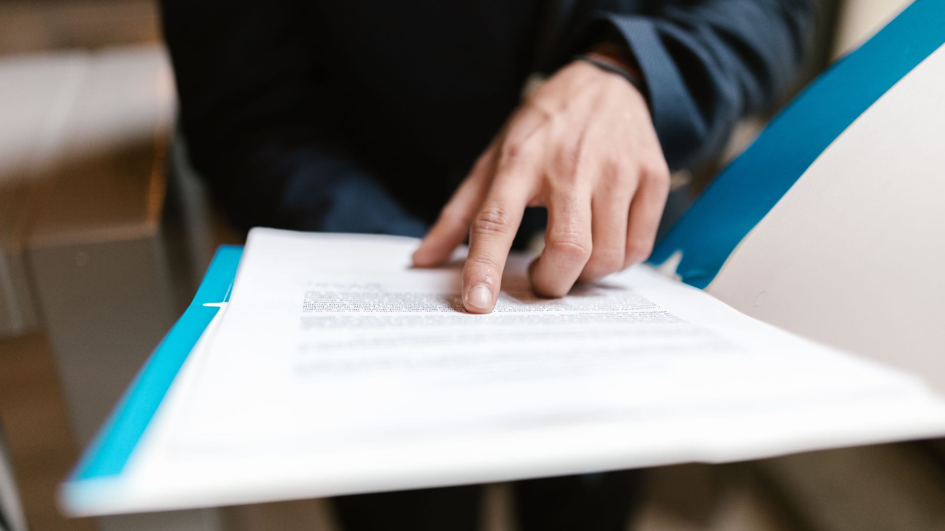 Close-up of a hand pointing at text on a business document in an office environment.