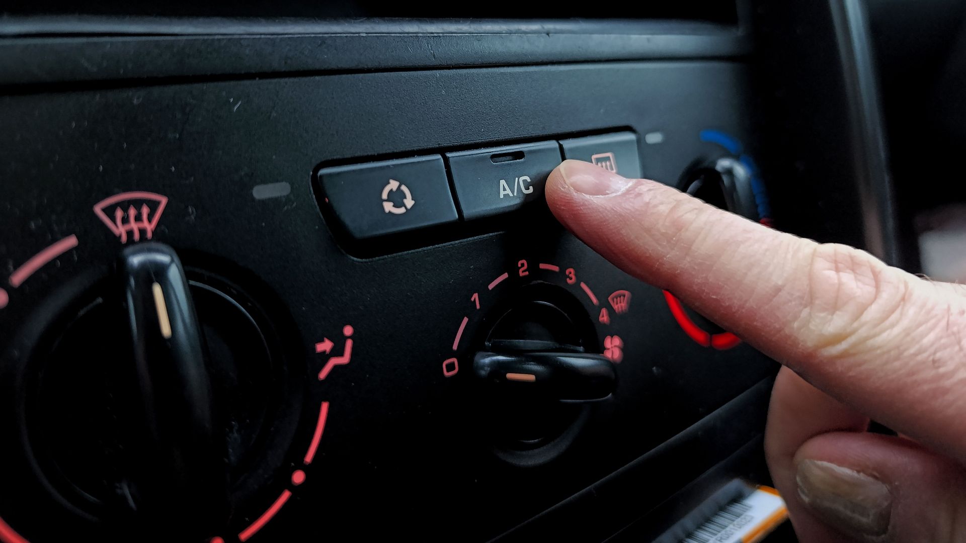 Close-up of a person adjusting a car's air conditioning system inside a vehicle cabin.