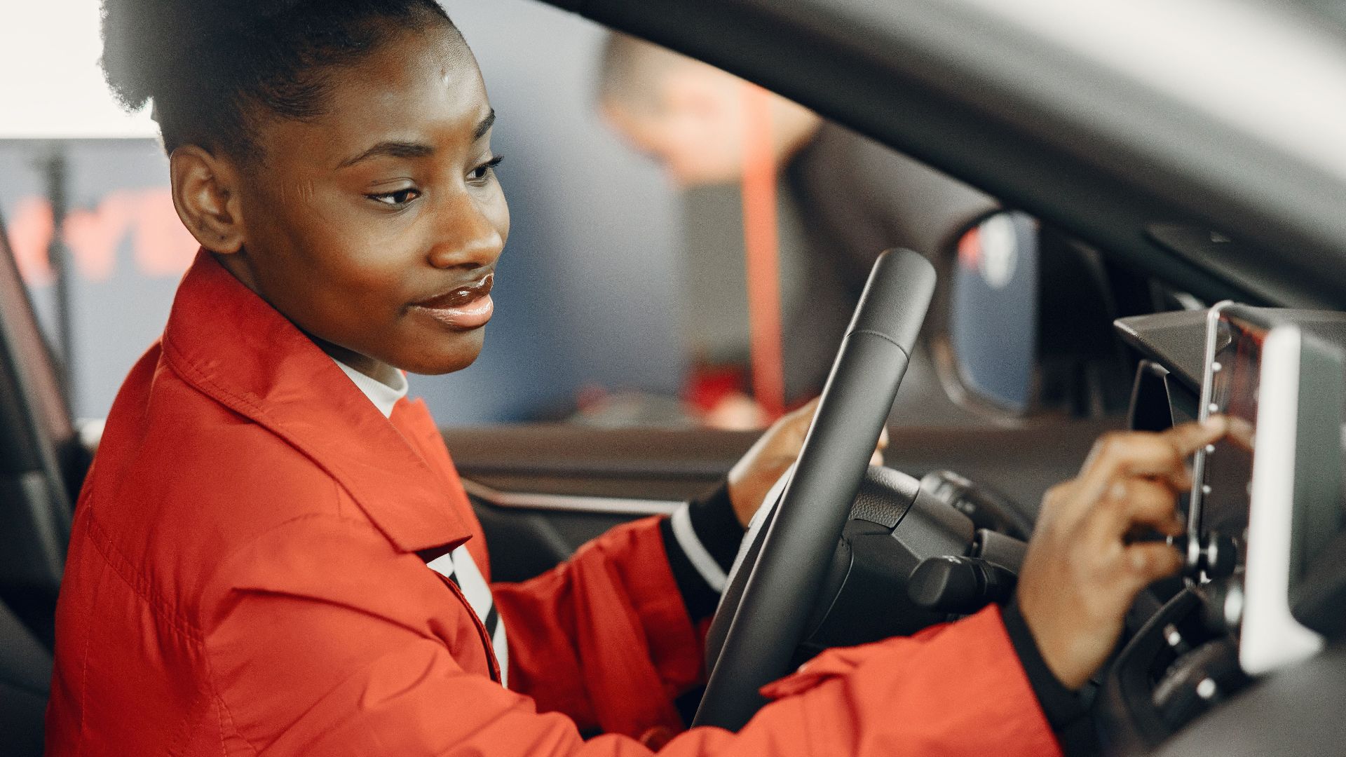 Young woman in red coat using touch screen in car interior.