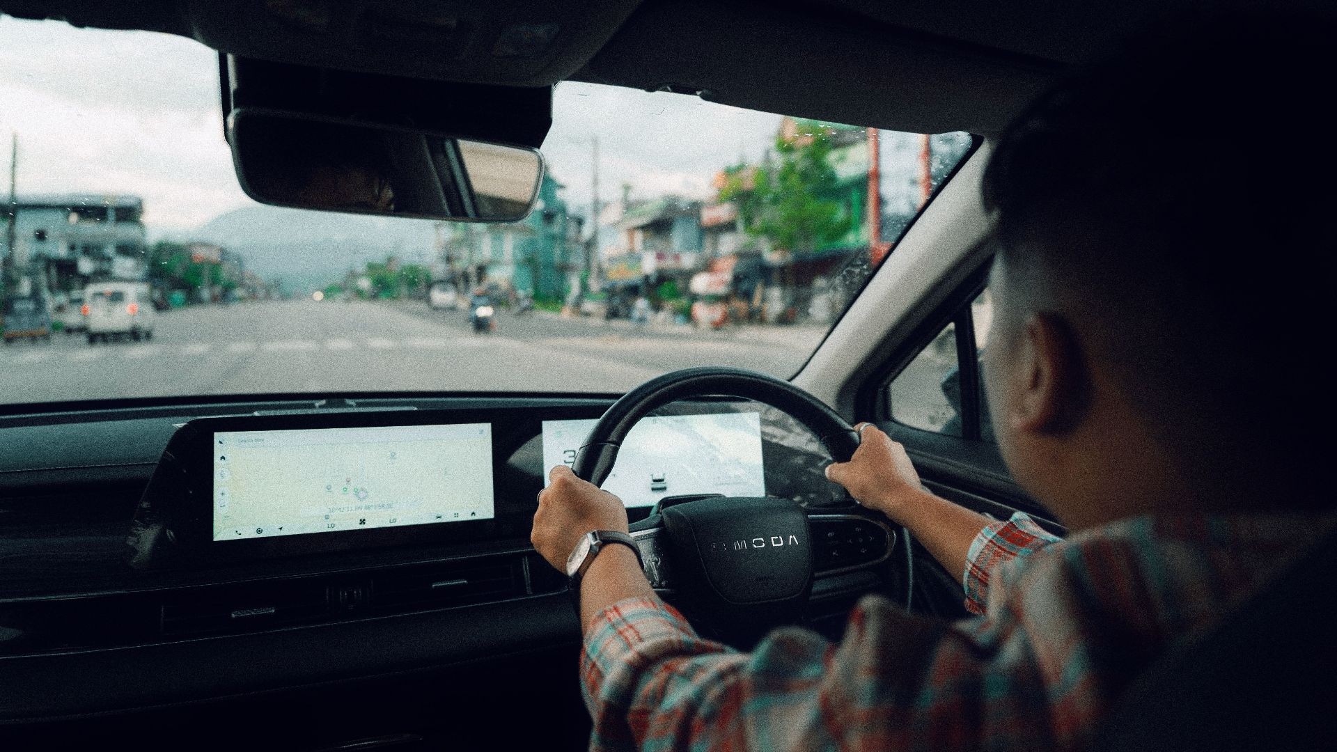 Person driving a modern car through town, showing dashboard and road view.