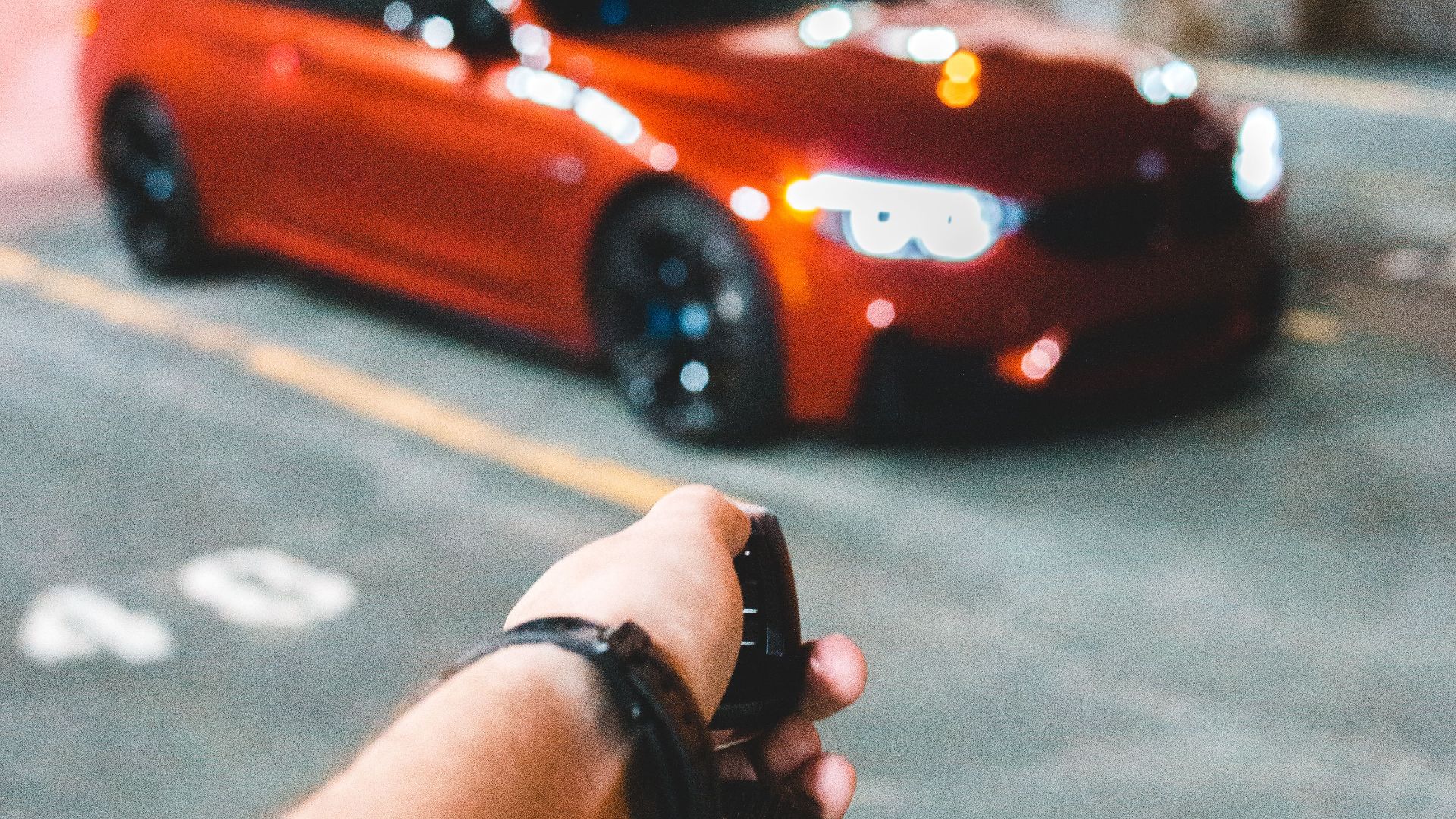 Crop hand of anonymous person using remote key to open red sport car on grunge parking