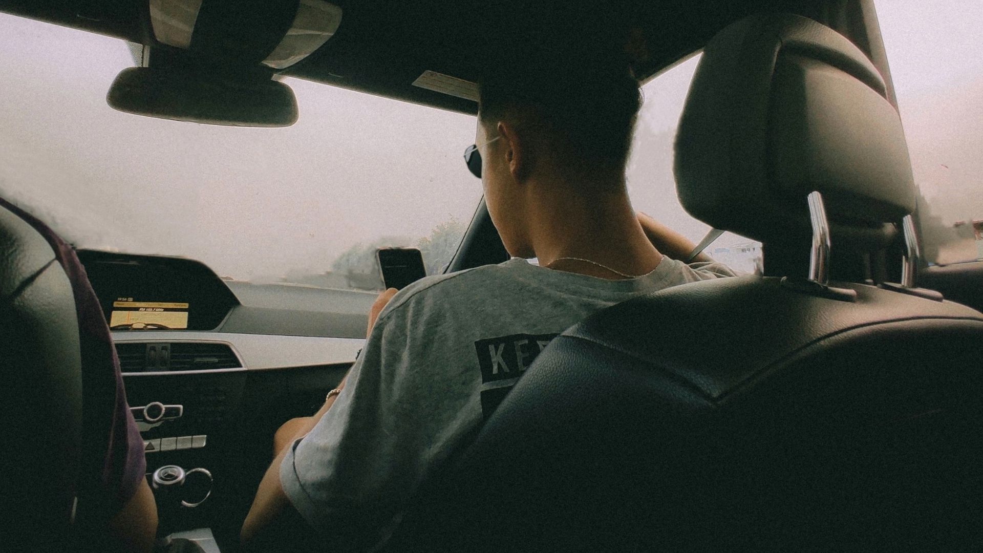 Back seat view of two people driving in a car on a cloudy day.