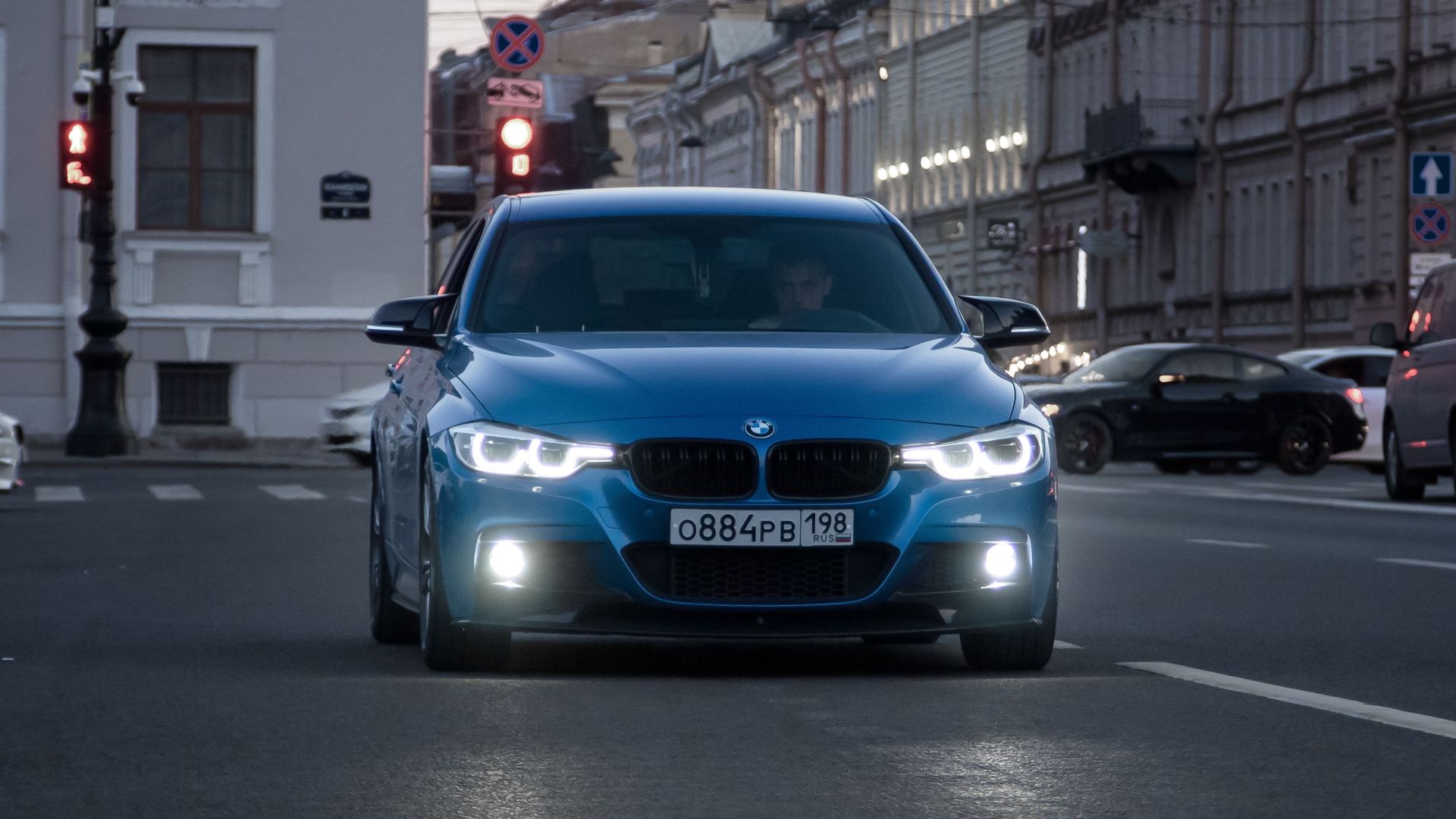 A blue car drives on a city street at dusk, showcasing urban life and motion.