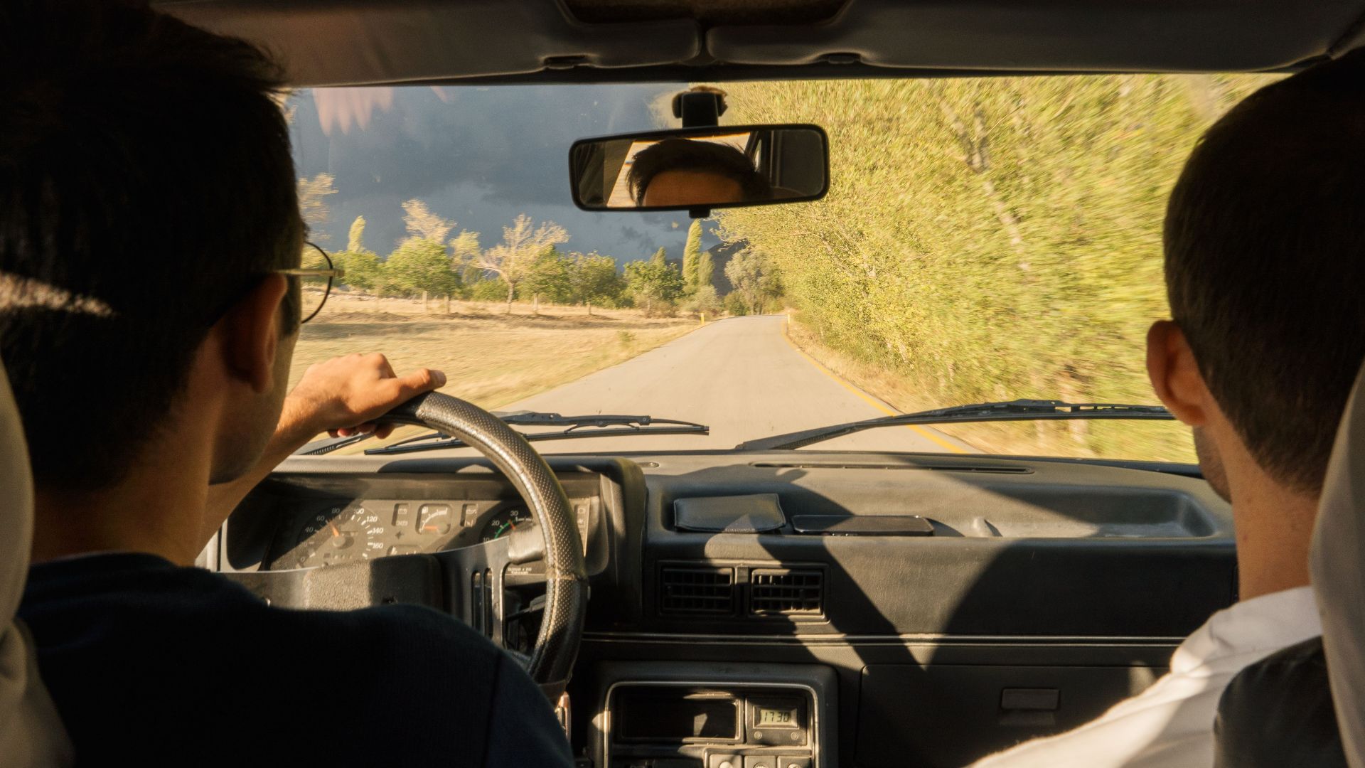 Two adults driving through scenic countryside near Merzifon, Turkiye, in a vintage car.