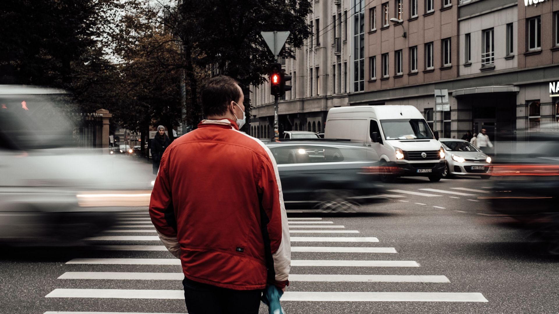 Man in red jacket at a busy pedestrian crossing in Riga, Latvia during the day.