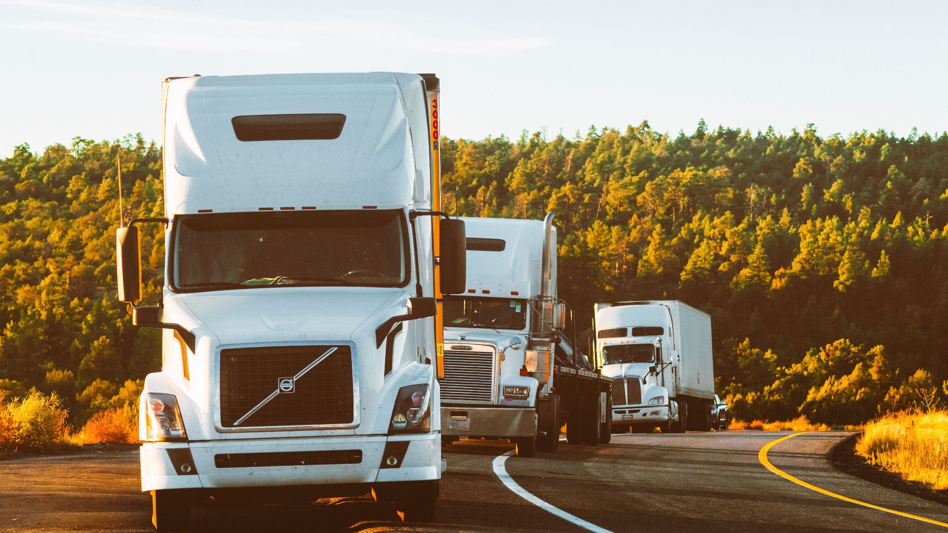 Three semi trucks driving on a highway through a forested landscape in Arizona.
