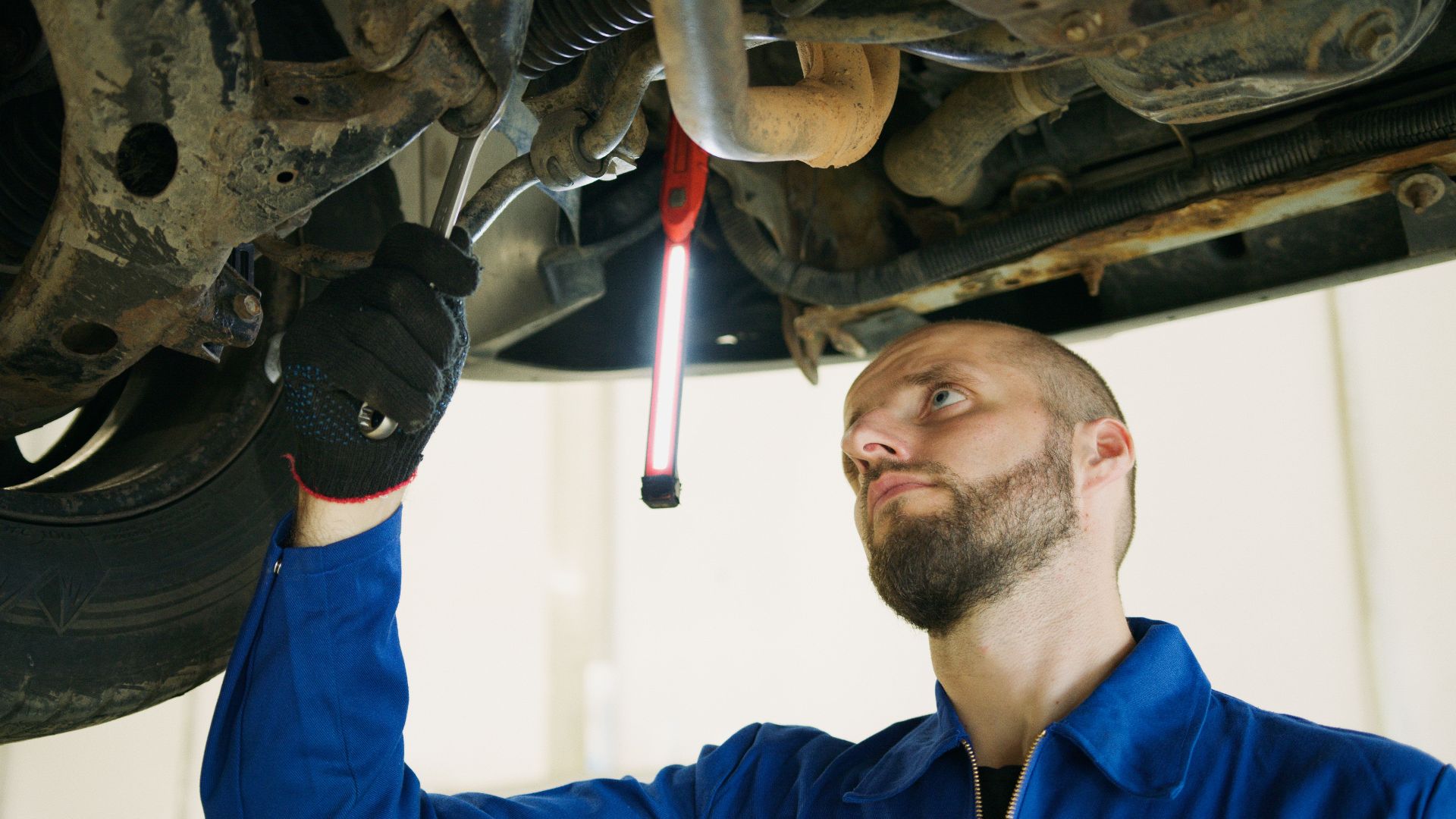 Mechanic focusing on vehicle maintenance under a car lift in a garage.