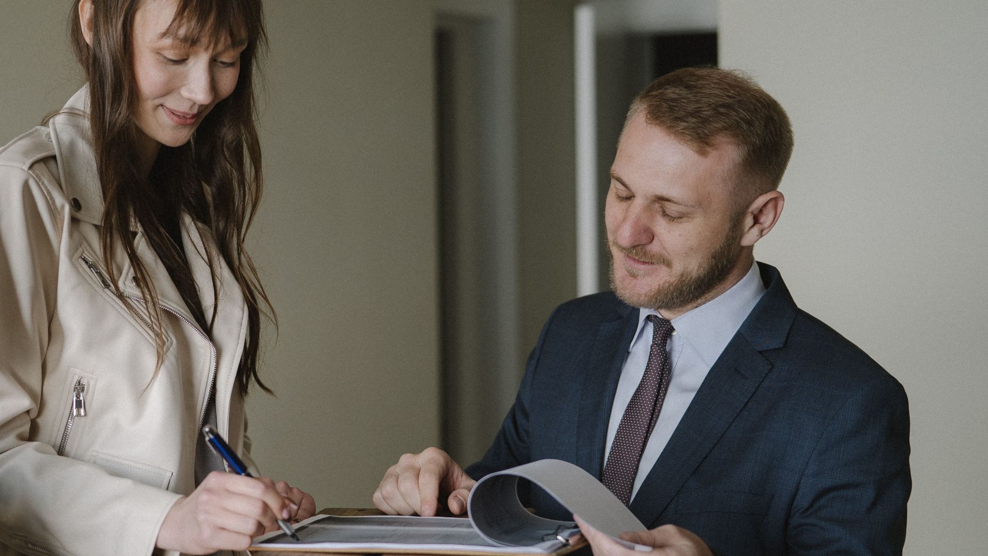 A couple signing real estate documents with a realtor inside a new apartment.