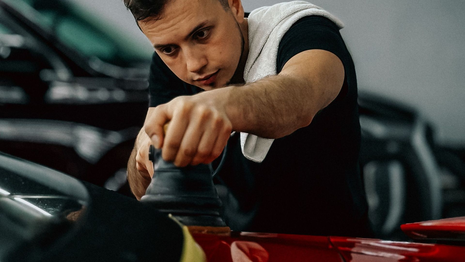 Focused man polishing a red car in a modern, well-lit workshop.