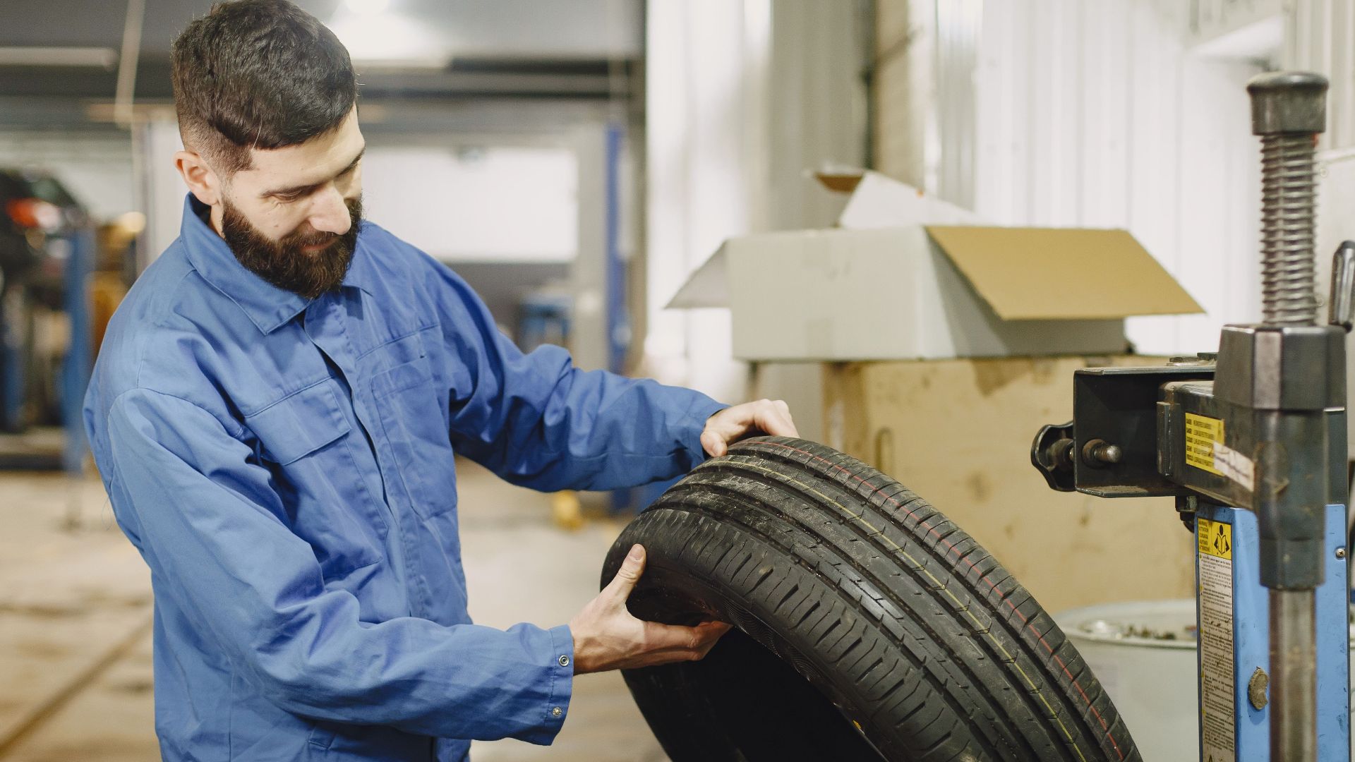 Mechanic in blue uniform examining a tire in an automotive garage.