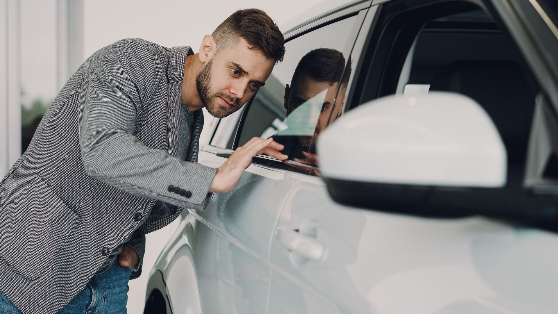 Man carefully examining a modern white car at a dealership showroom.