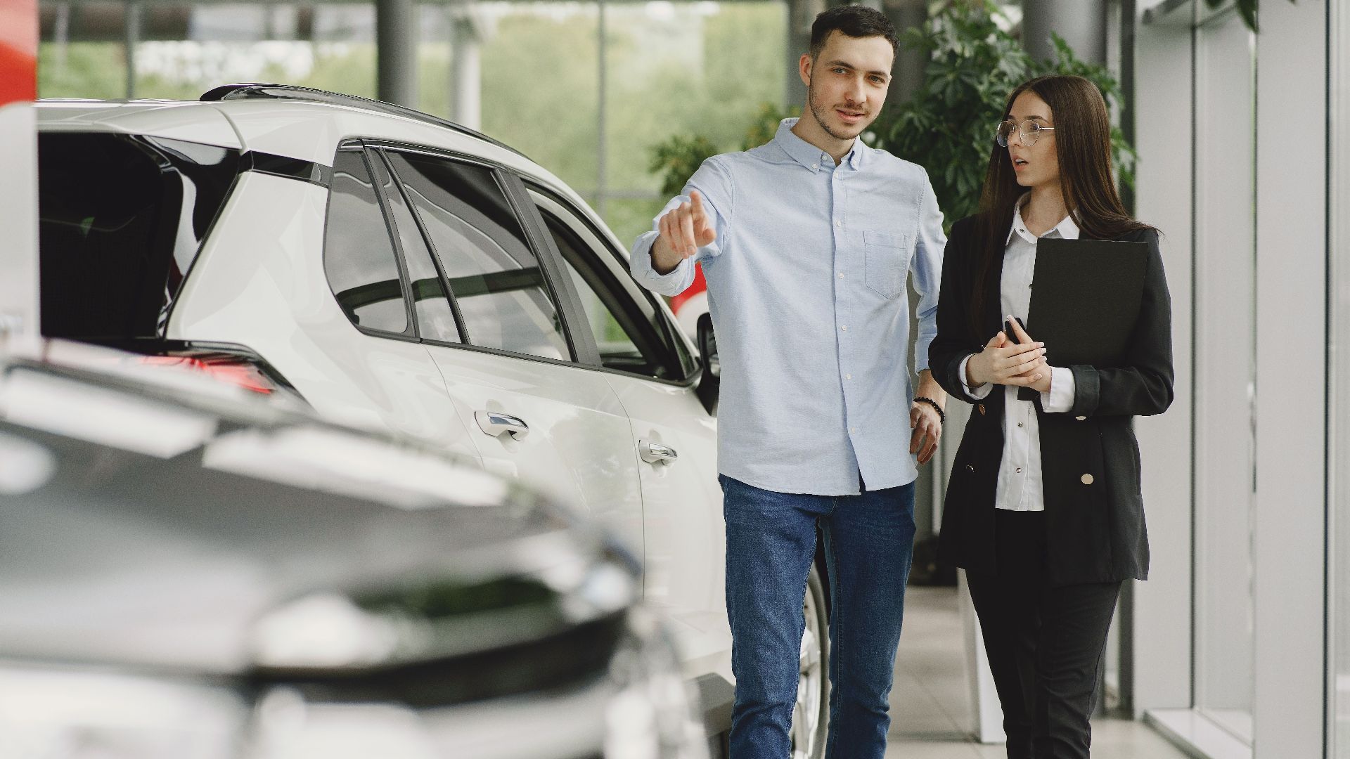 Customer and salesperson discussing a vehicle inside a modern car dealership showroom.