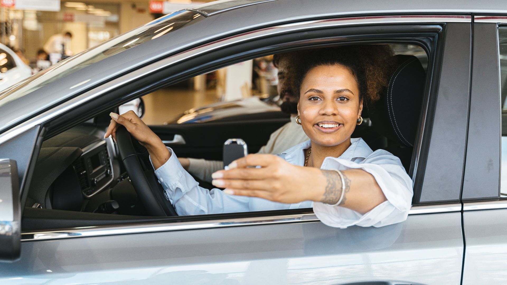 Smiling woman sitting in her new car holding keys, celebrating purchase.