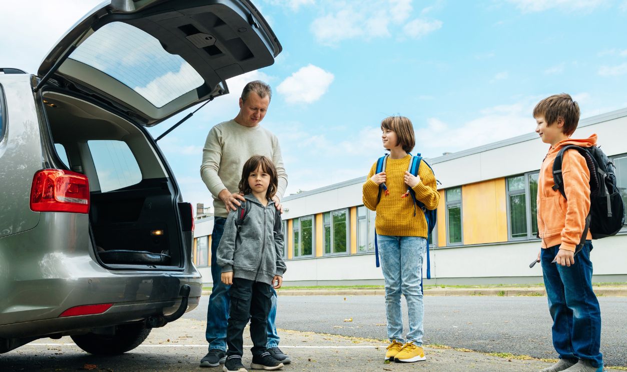 Back to school. Dad escorts his children to school, father takes school bags out of the car. Parental care for children