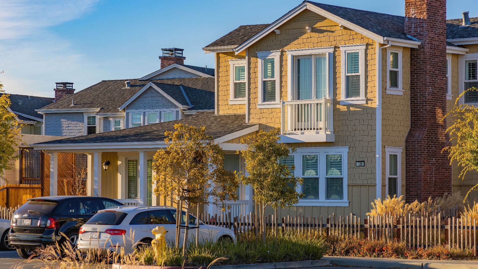 A picturesque suburban house with cars parked outside under a clear sky.