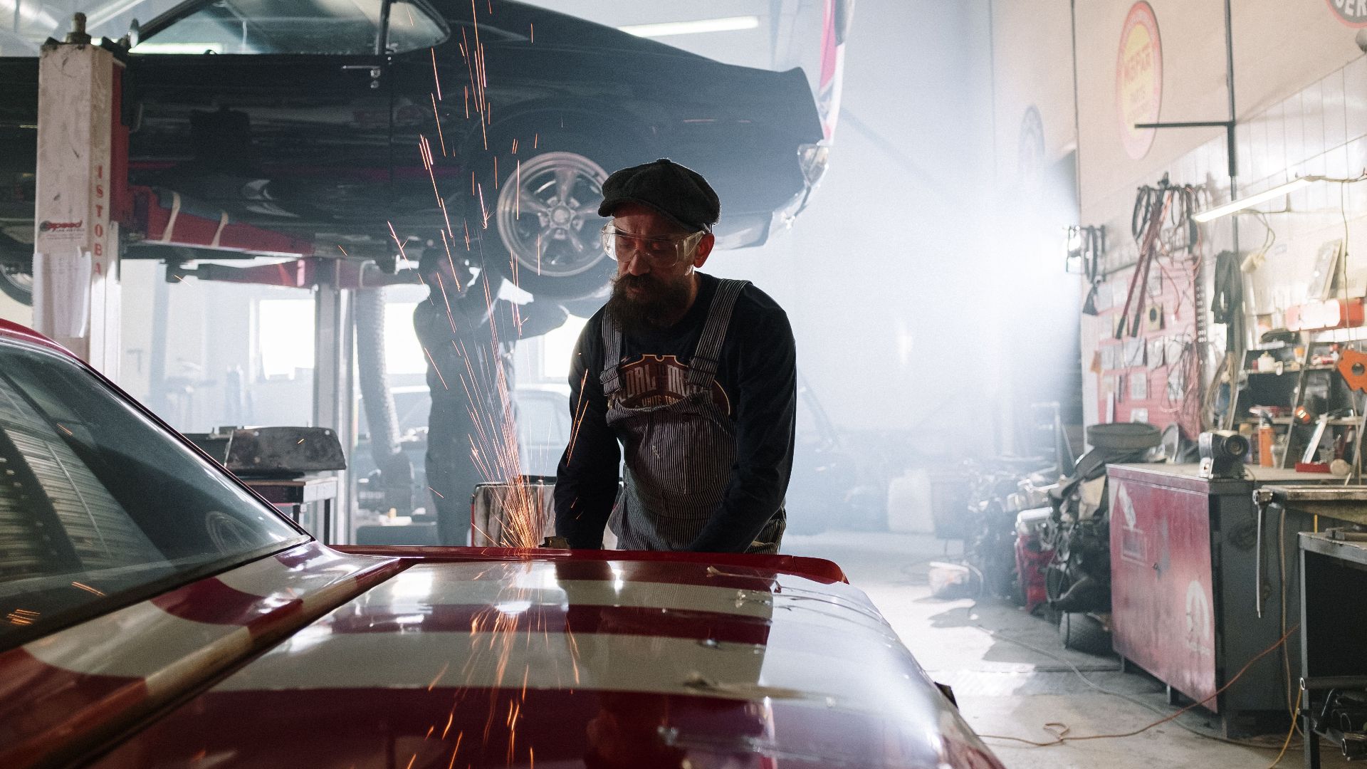 Mechanic skillfully repairs a car in a bustling automotive workshop with sparks flying.