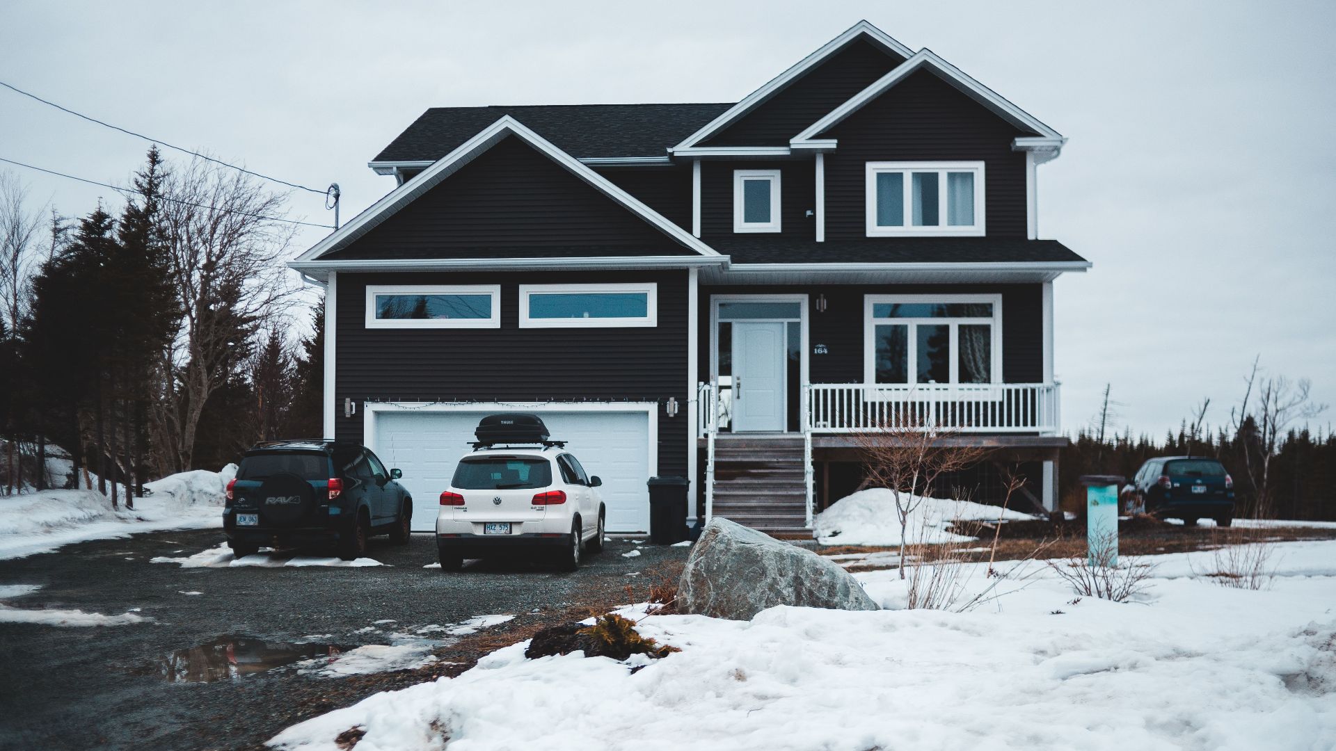 Facade of cottage with cars at garage in countryside covered with snow in winter season