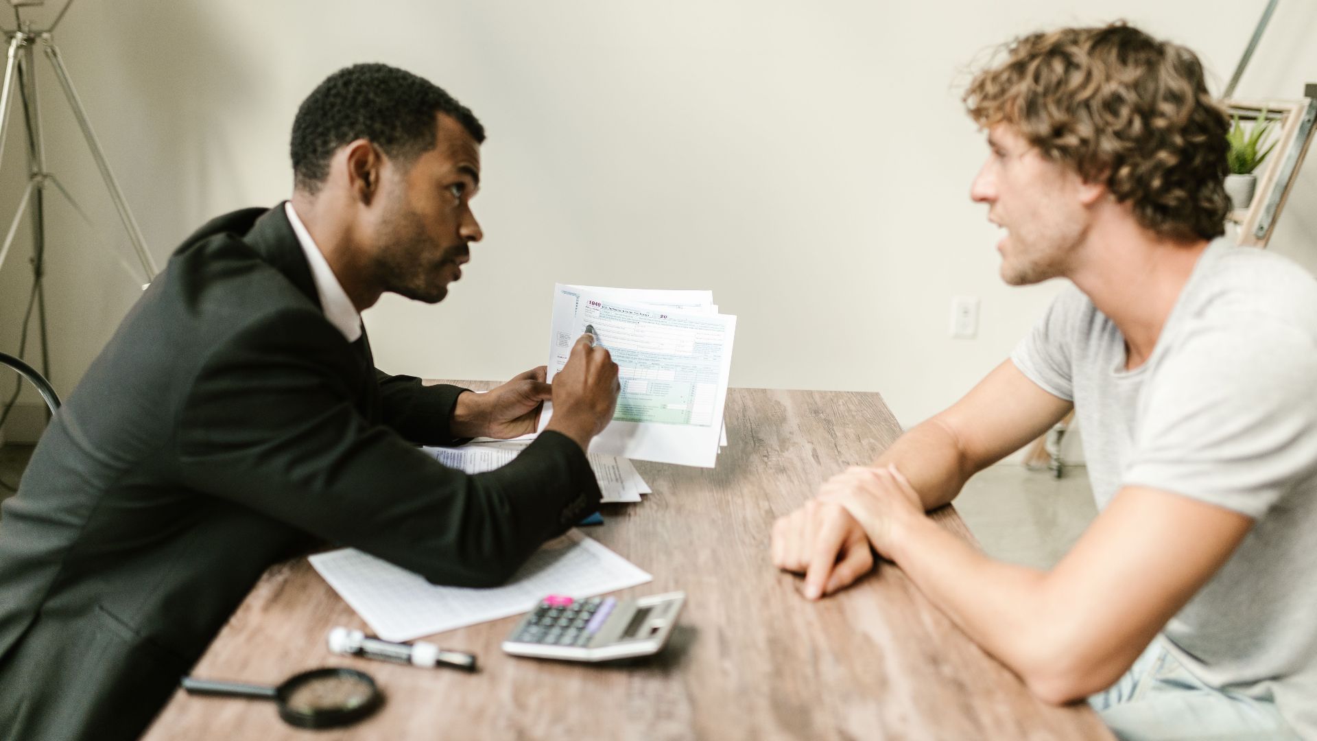 A financial advisor discusses paperwork with a client at a desk in a modern office.