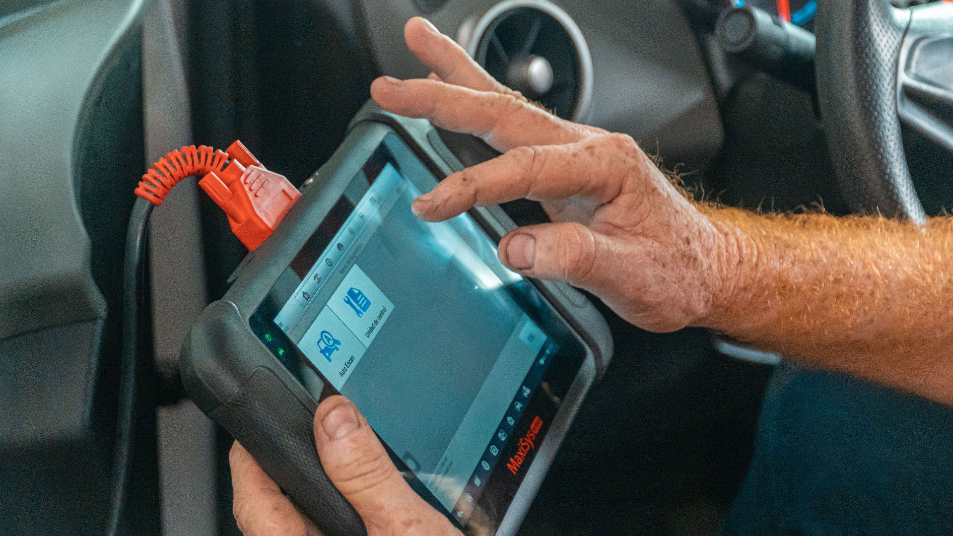 Mechanic using a diagnostic tool inside a car to check for engine issues and ensure proper maintenance.