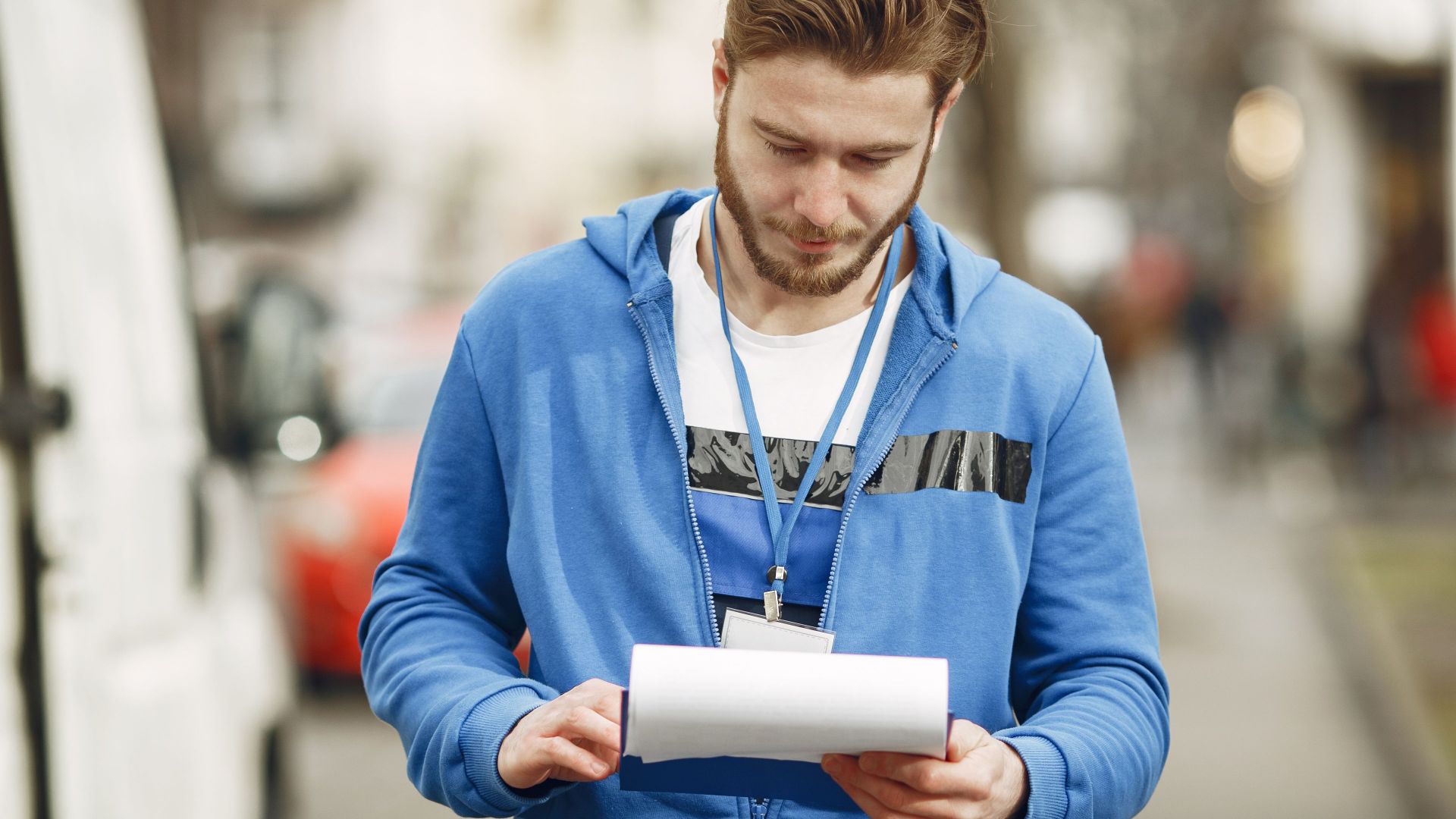 A delivery worker in blue uniform reading documents on a city street during the day.