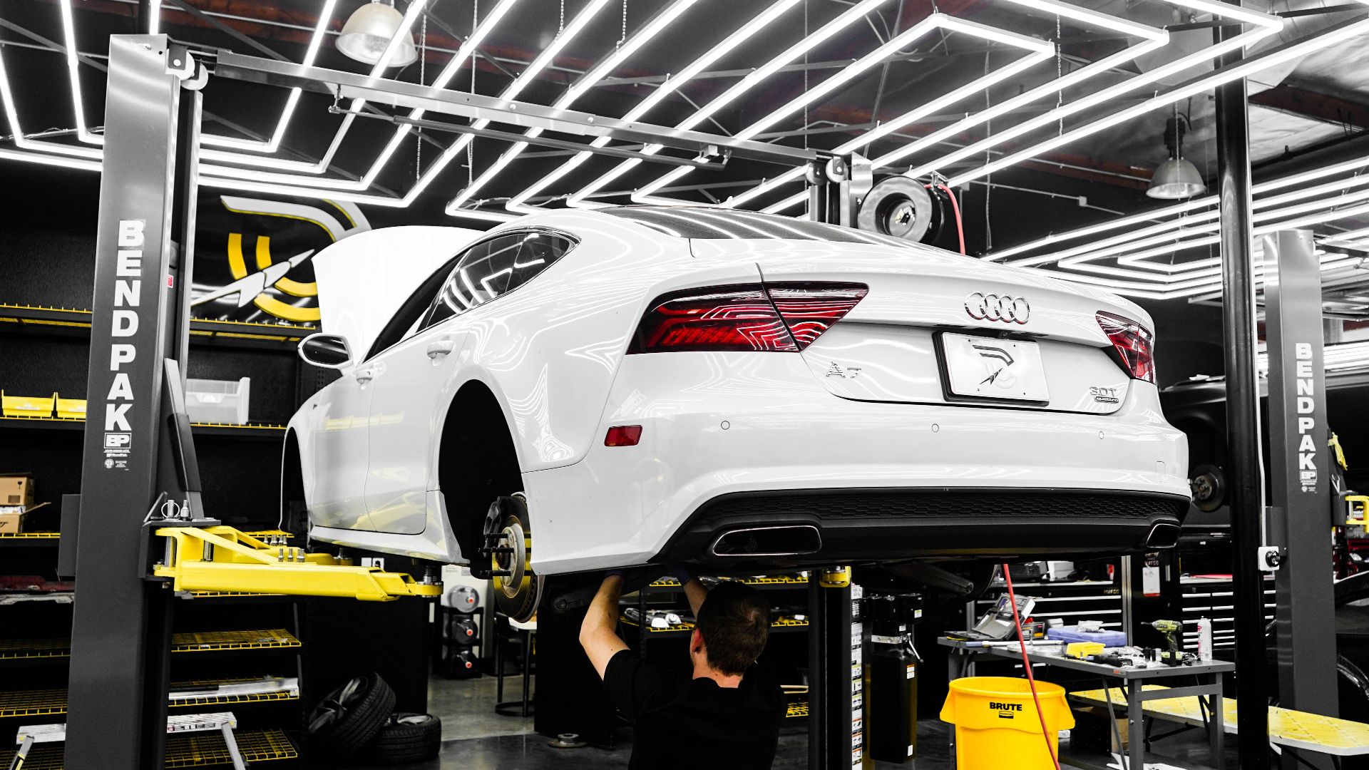 White luxury car being serviced by mechanic in a modern garage setting.