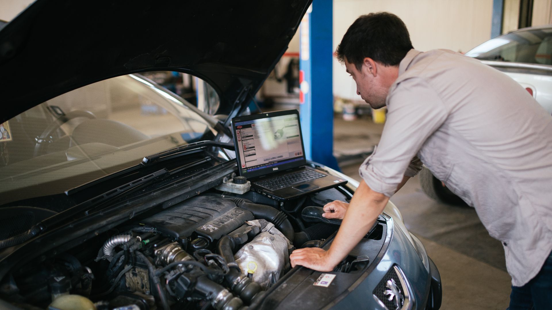 Young mechanic with laptop doing car diagnostic at automobile repair shop close