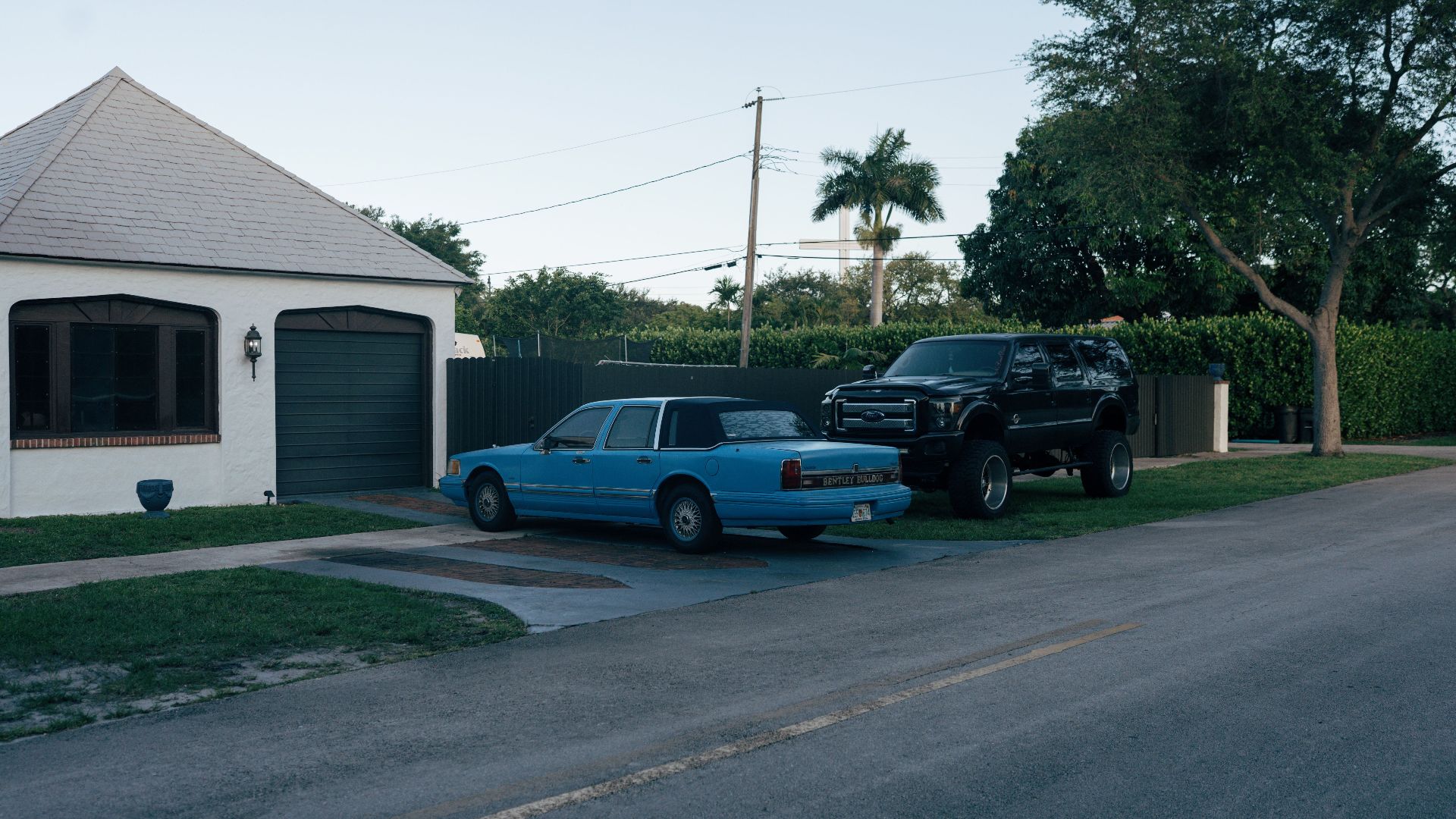 Classic and modern cars parked on a quiet residential street in a suburban neighborhood.