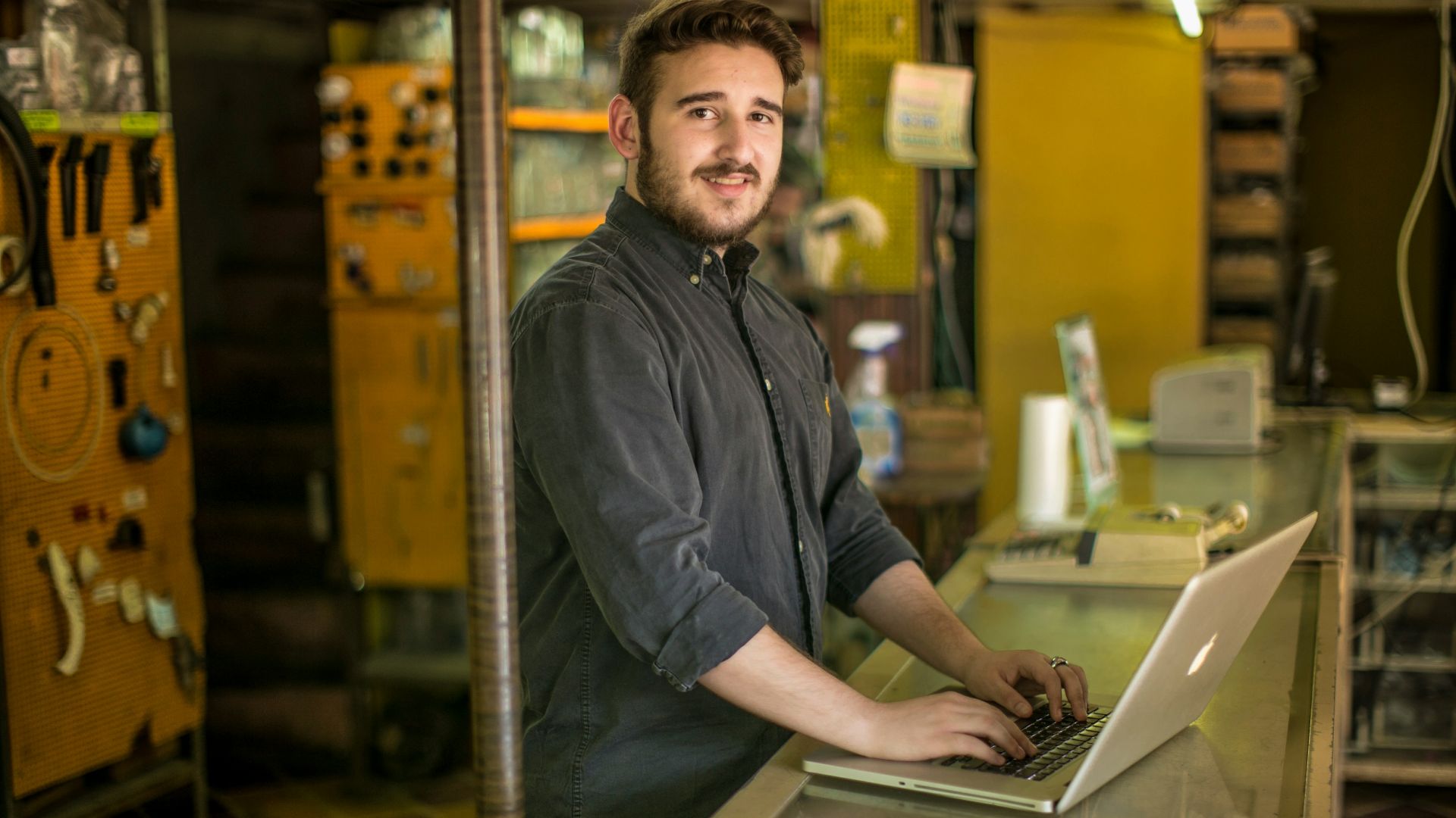 man standing and smiling while using MacBook