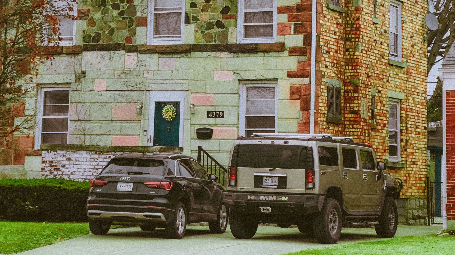 Quaint green brick house with colorful facade and parked cars in suburban setting.
