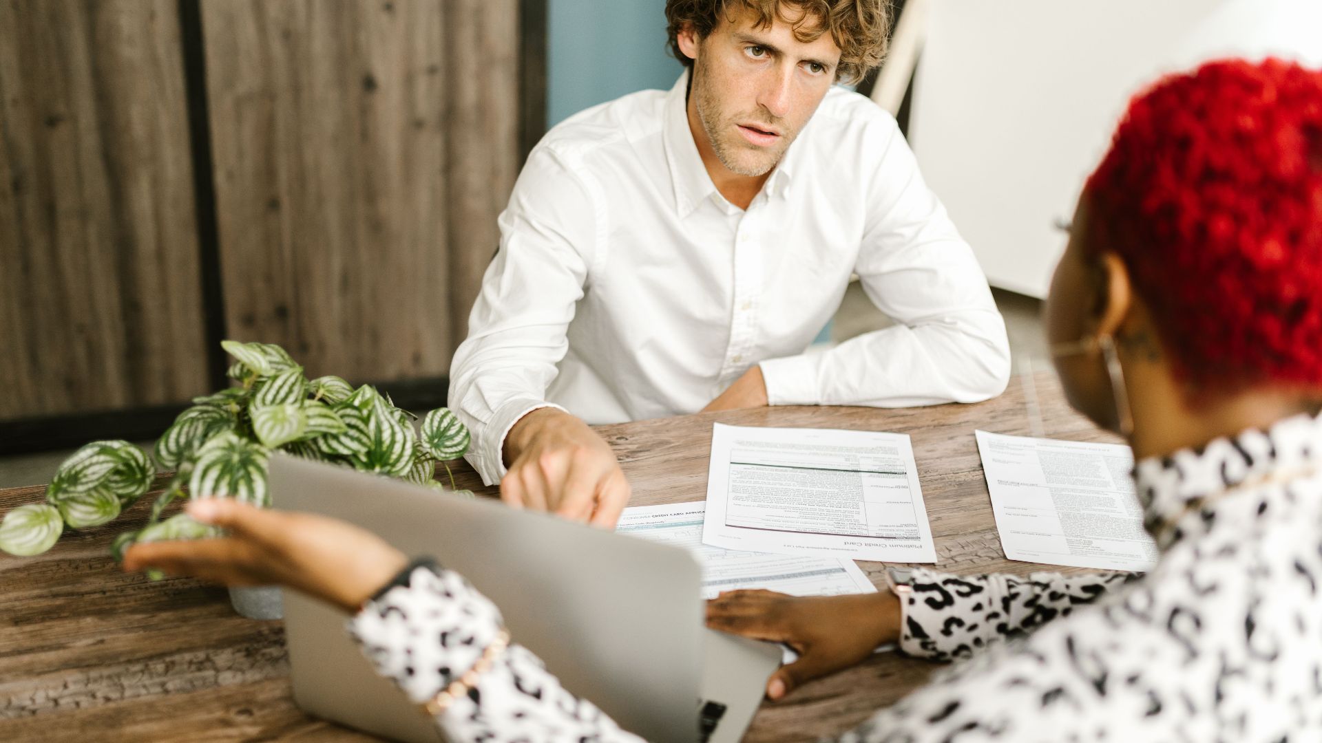 Business professionals discussing documents at a wooden table in an office setting.