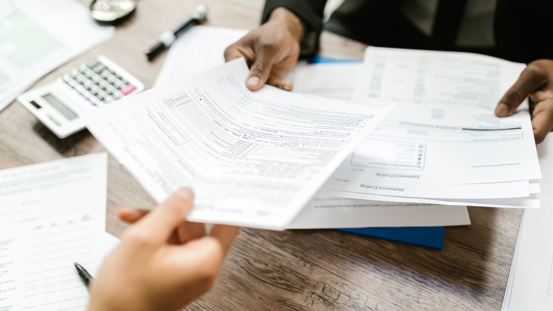 Two professionals exchanging documents in an office setting, focusing on paperwork and data analysis.