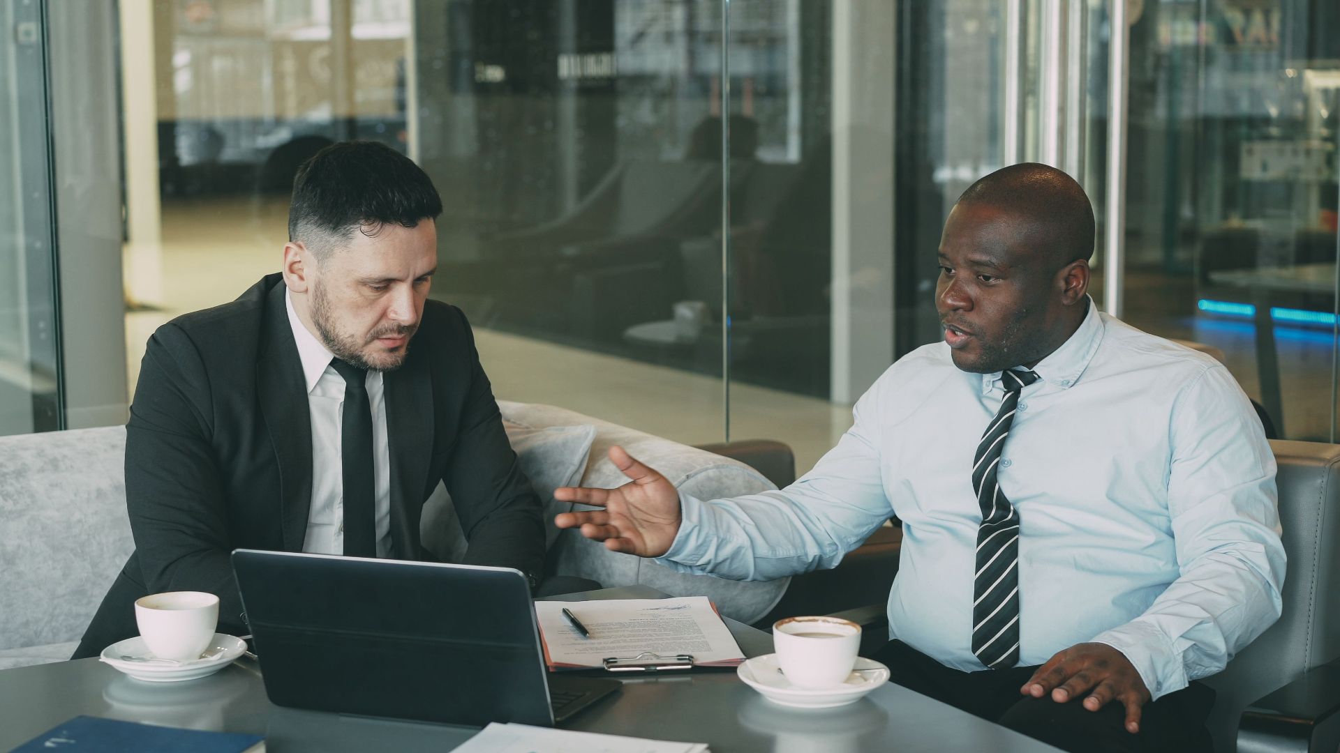 Two businessmen in a strategic discussion over coffee in a modern office setting.
