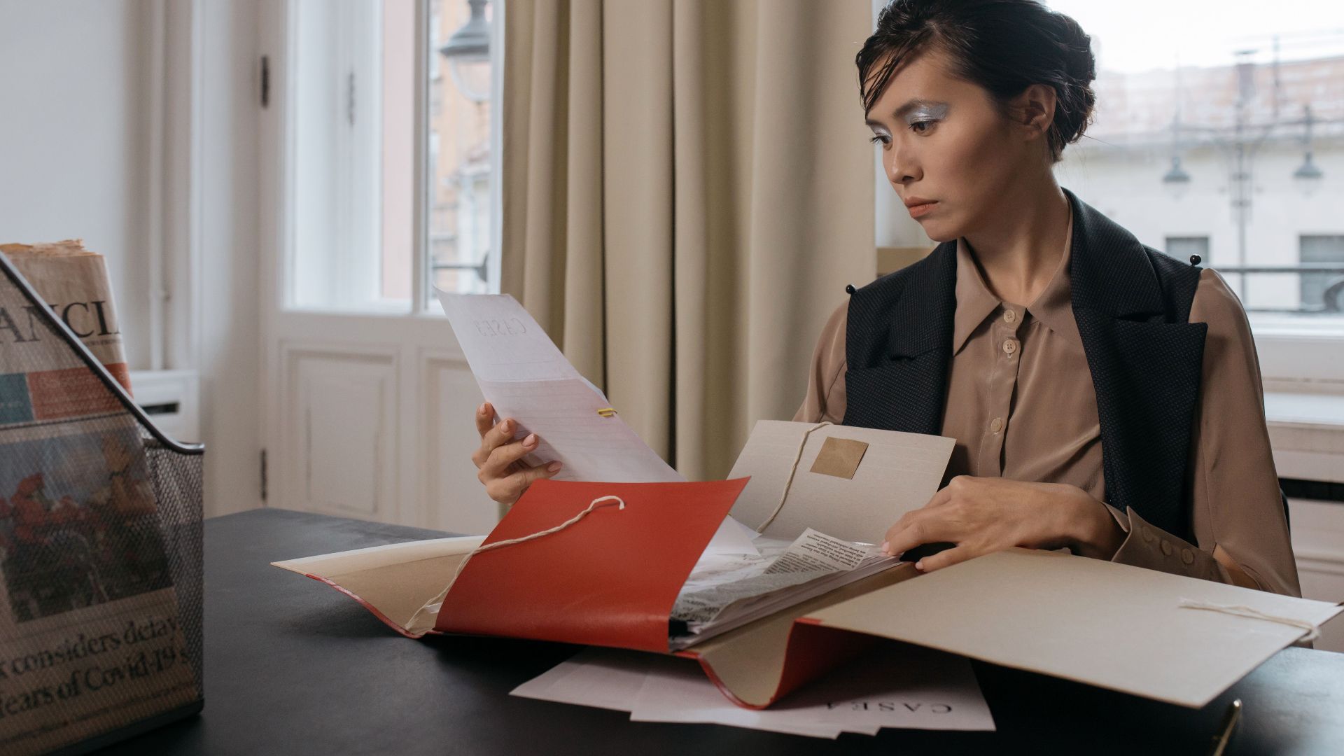 Businesswoman in an office setting reviewing important documents from a red folder with focus and determination.
