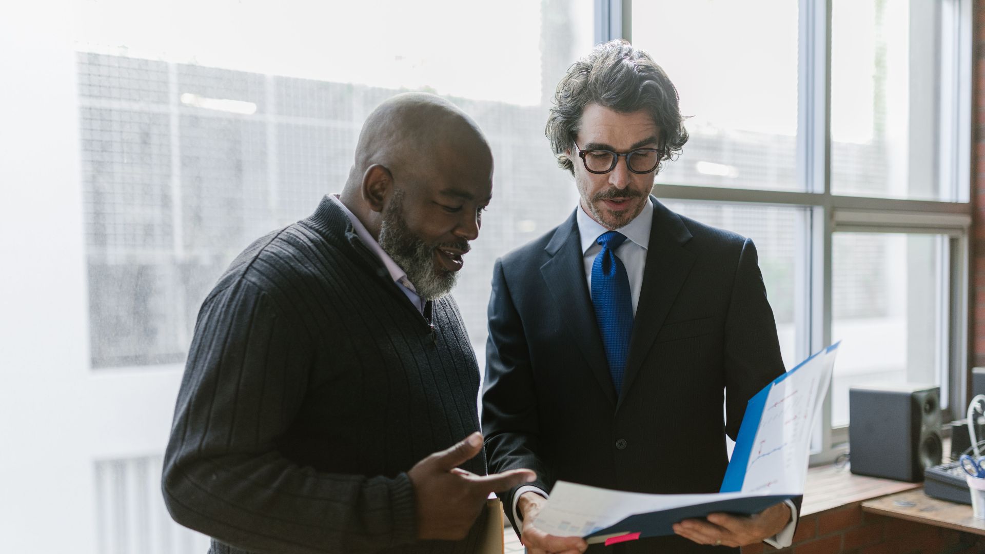 Two businessmen discussing and reviewing documents in a modern office setting.