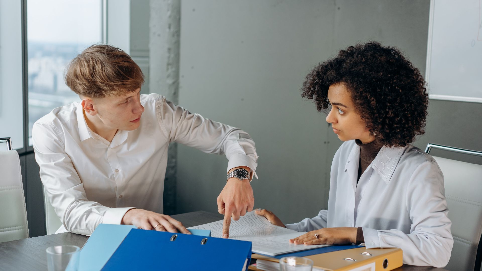 Professional workplace discussion between colleagues reviewing documents at an office table.