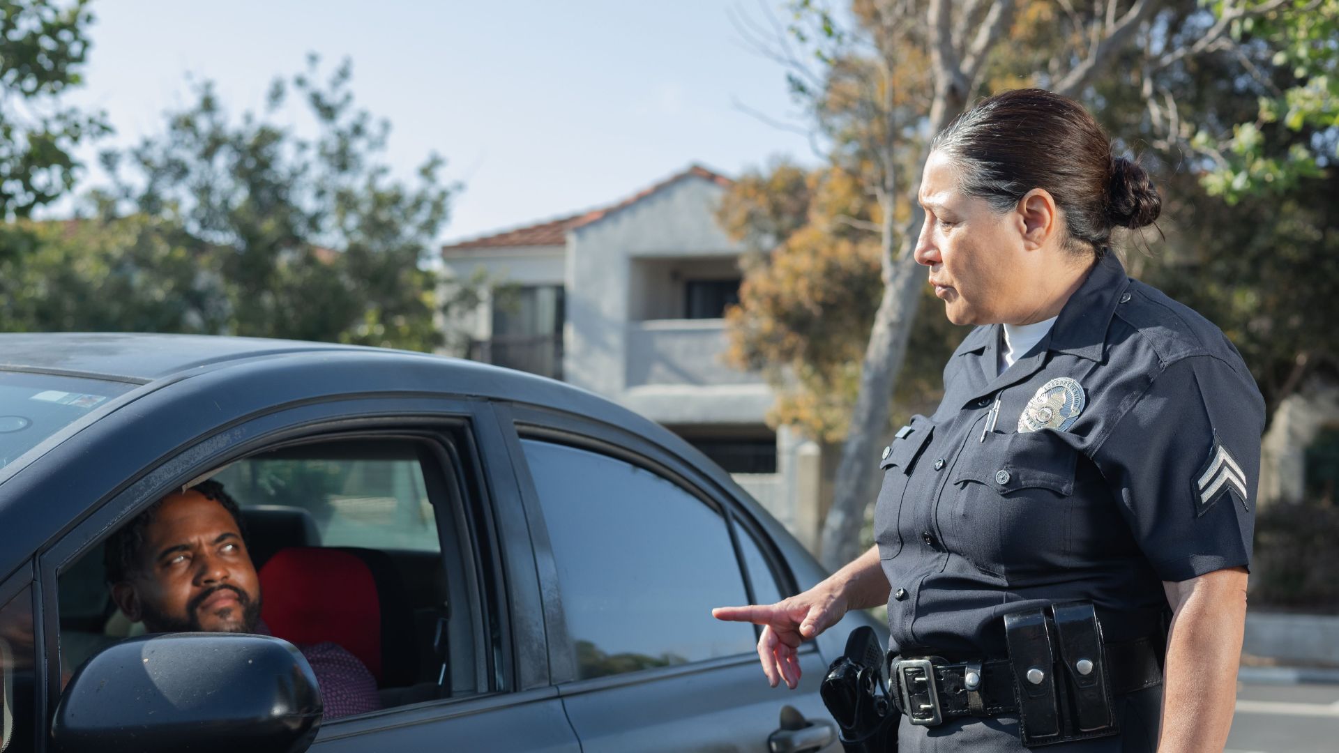 A police officer interacts with a driver during a daytime traffic stop on a residential street.