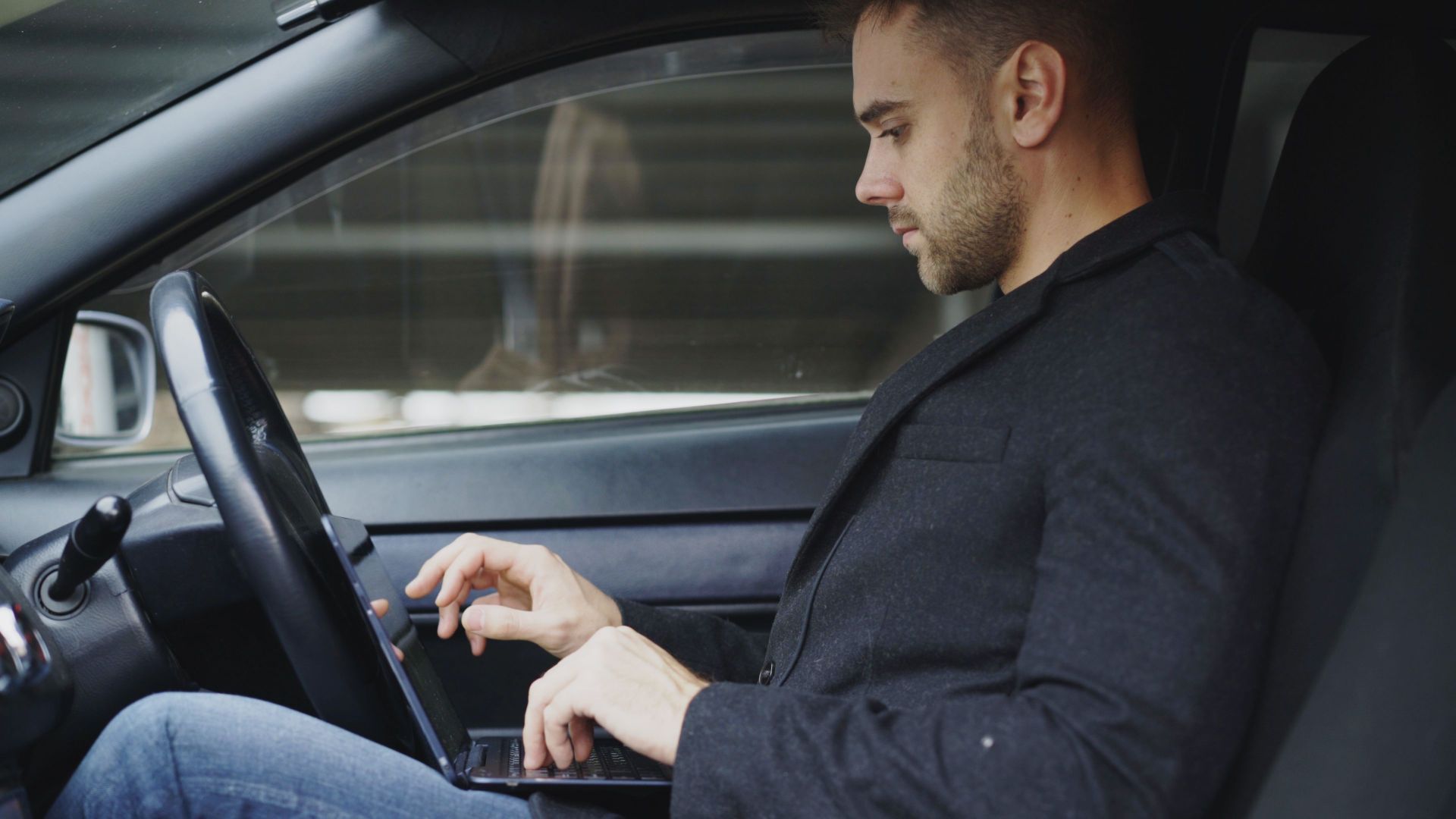 Focused businessman using laptop in car, multitasking and working on the go.