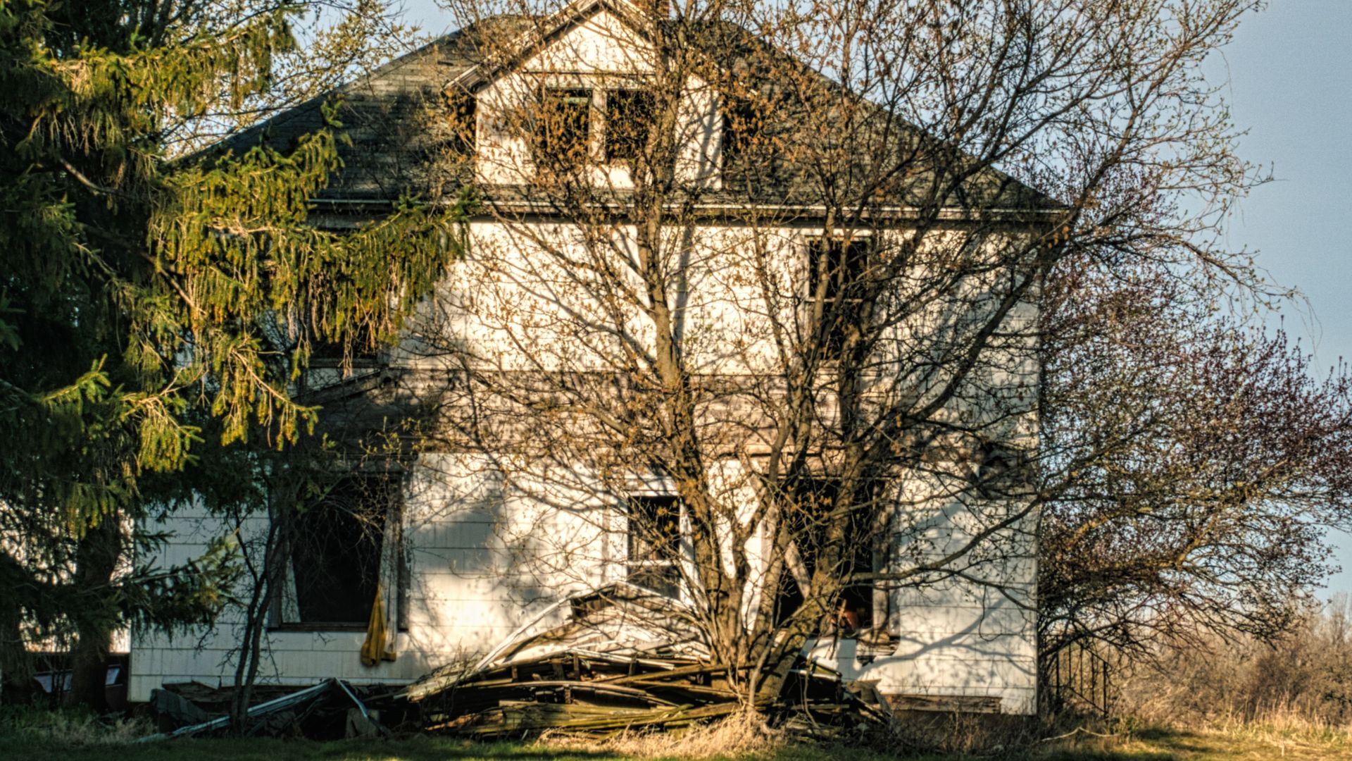 An old abandoned house stands amidst bare trees and grass in Minnesota, USA.