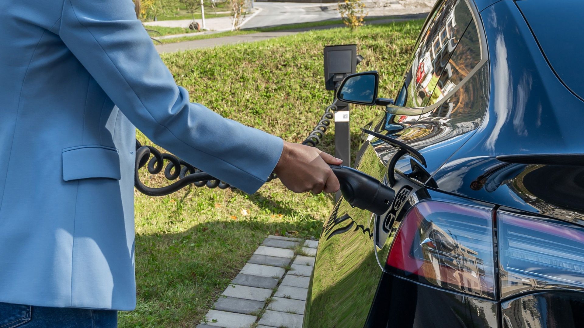 Person connecting an electric car to a charging station outdoors, showcasing green energy transition.
