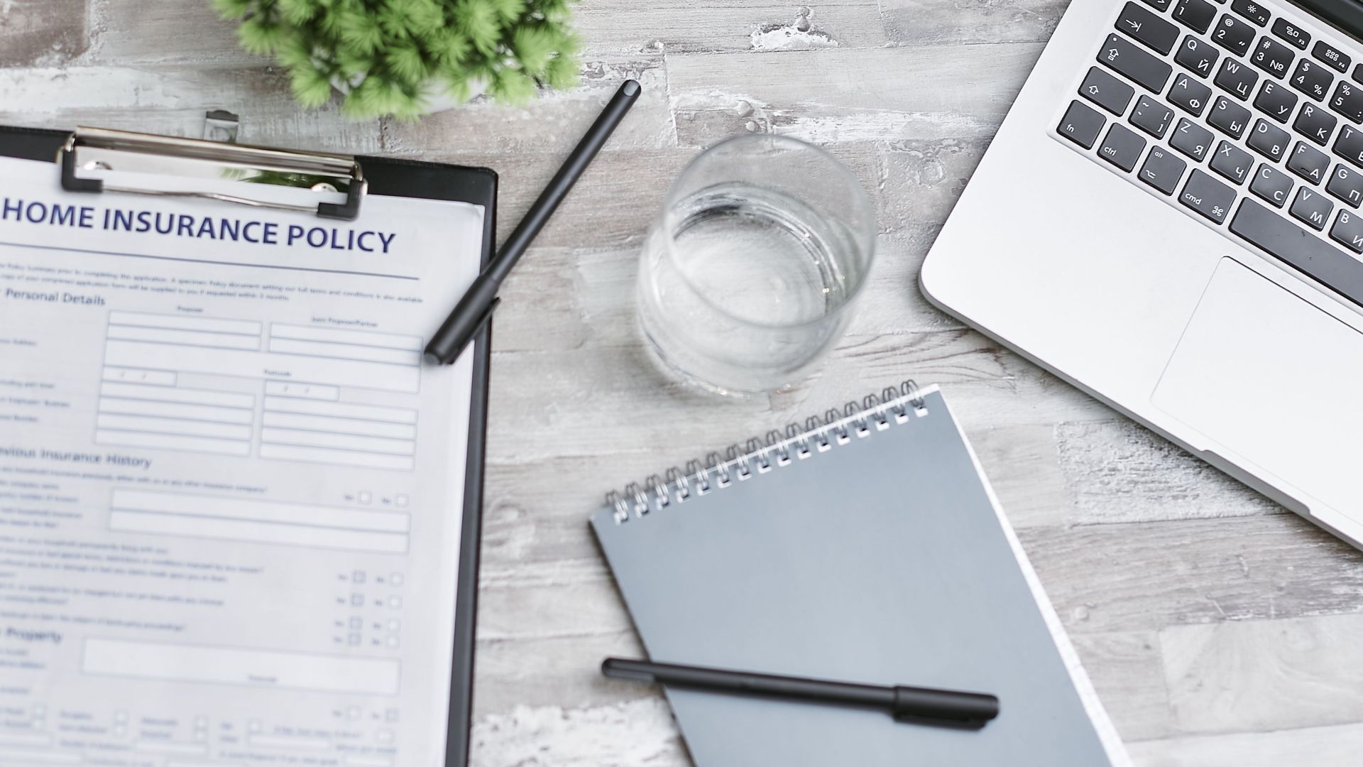 Flat lay of a workspace with a home insurance policy, laptop, and notebook on a desk.
